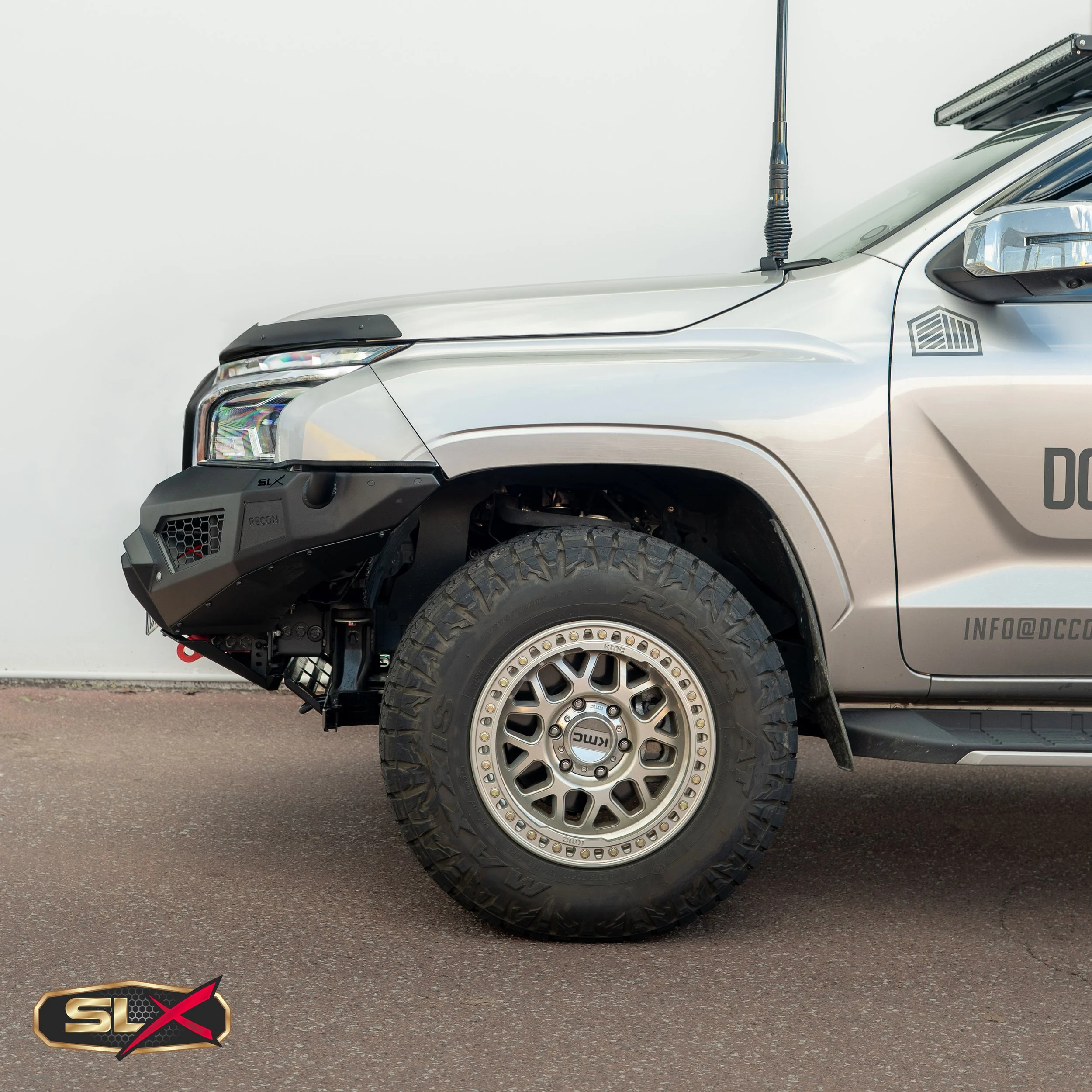 Close-up of the front side of a silver off-road vehicle with large rugged tires and a black bumper with 'SLX' branding.