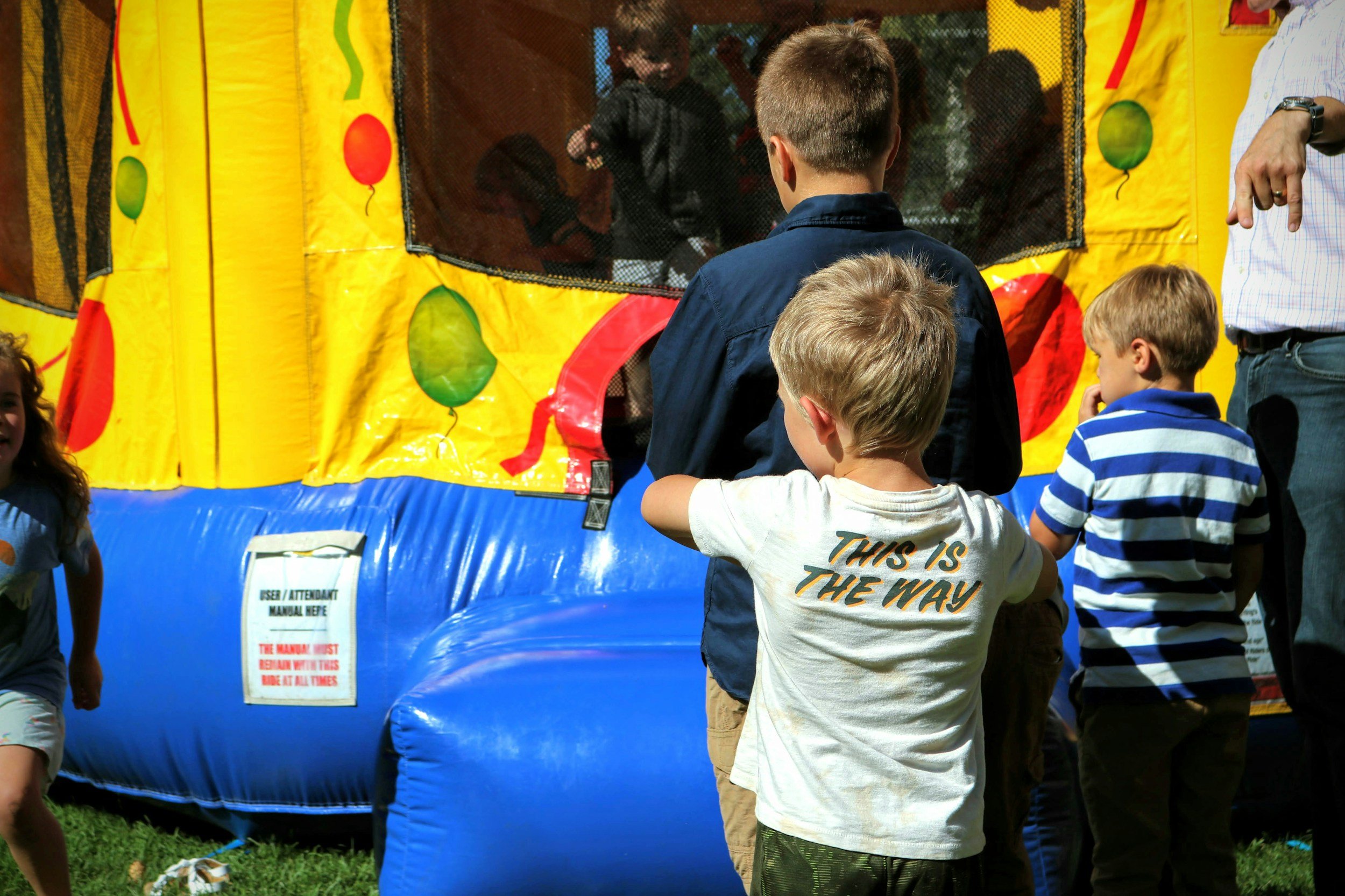 Happy children gathered around a large, colorful bounce house rental from Velvet Party Rentals in Washington MI, waiting their turn to jump during a backyard birthday party.