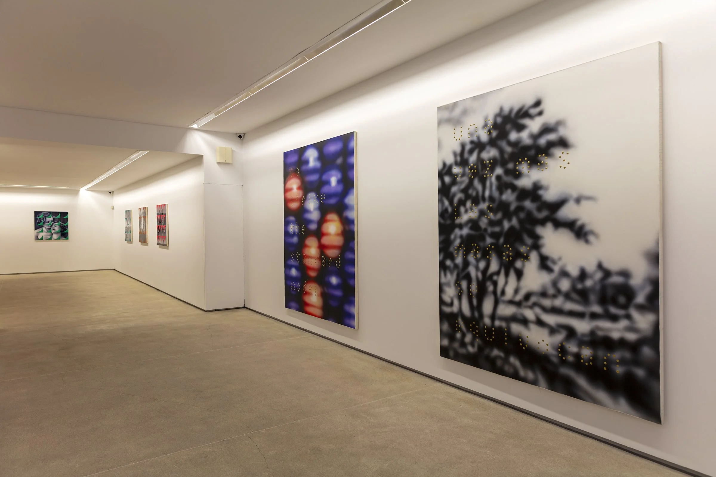 Galería de arte con varias pinturas abstractas en paredes blancas, iluminadas por luz artificial del techo.