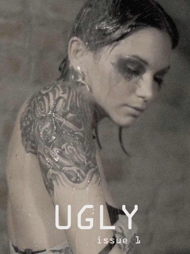 A black and white photo of a woman with dark makeup and tattoos, looking down. The text overlay reads "UGLY issue 1."