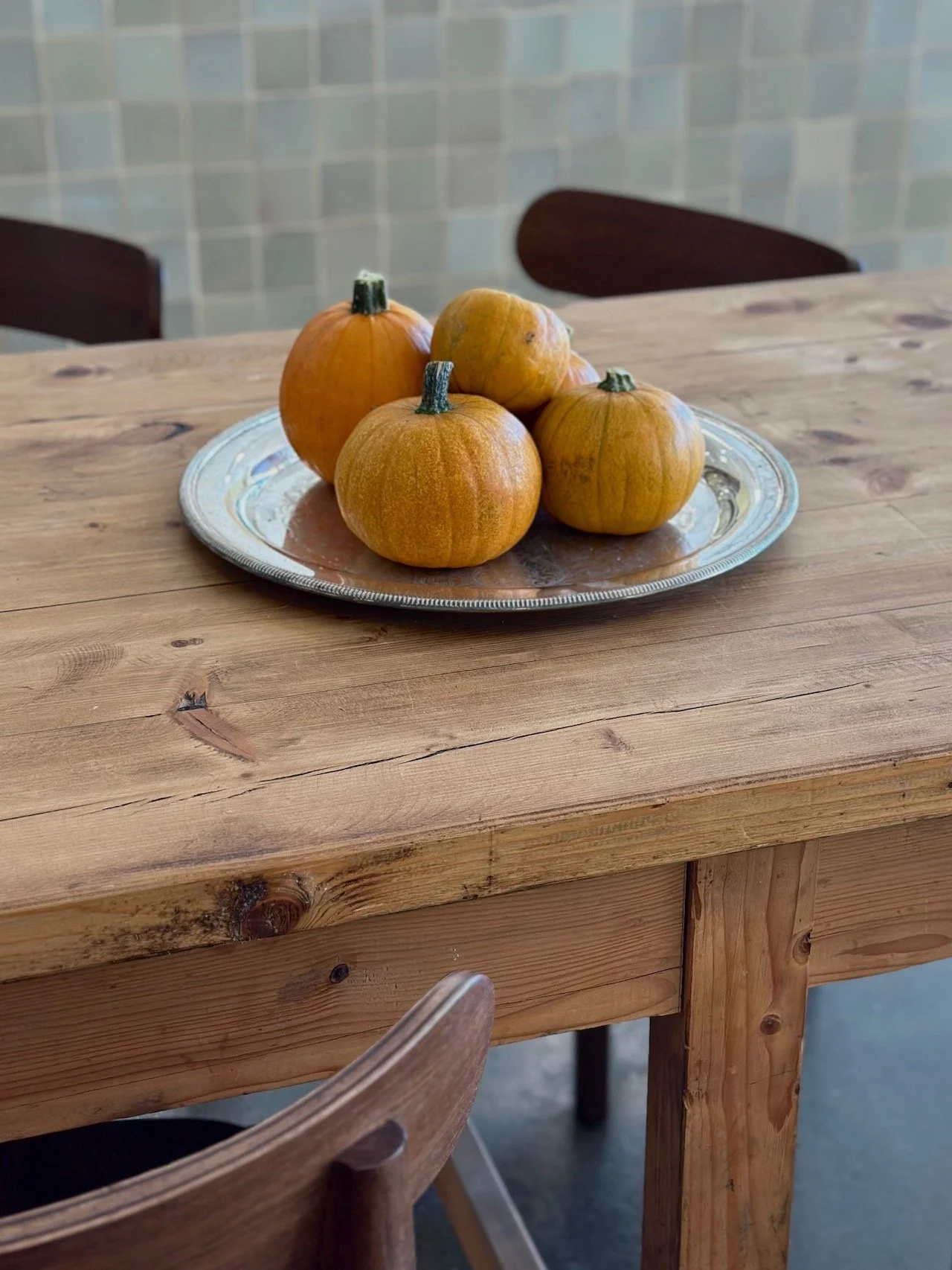 Four small pumpkins on a silver platter on a wooden table.