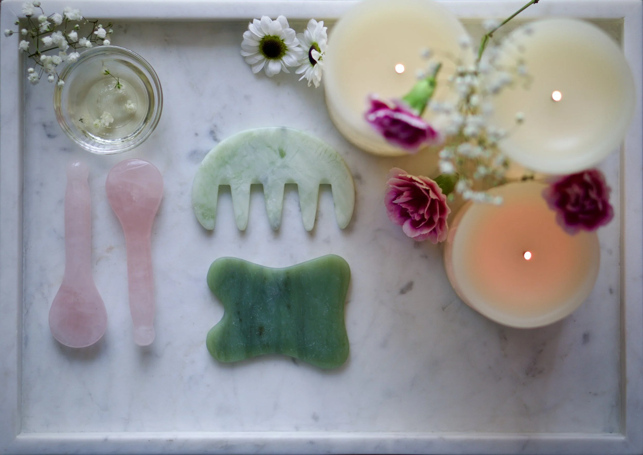 Decorative setting on a marble tray with candles, flowers, and soap or bath items including pink, green, and white soap shaped like animals and a comb, accented with candles and small flowers.