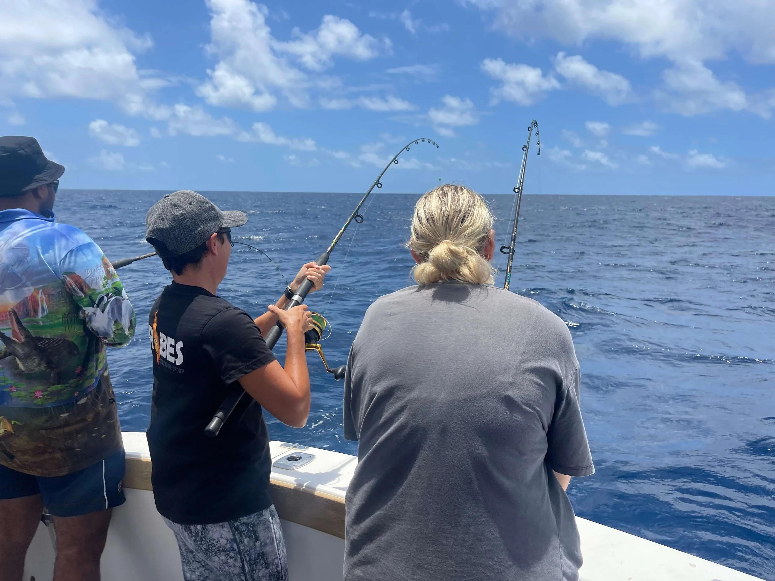 People fishing on a boat in the ocean under a blue sky with scattered clouds.