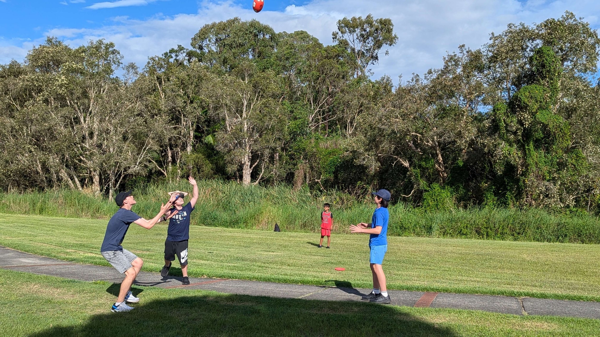 Children playing catch on a grassy field with trees in the background.