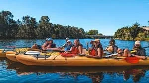 Group of six people paddling a yellow kayak on a lake under a clear blue sky