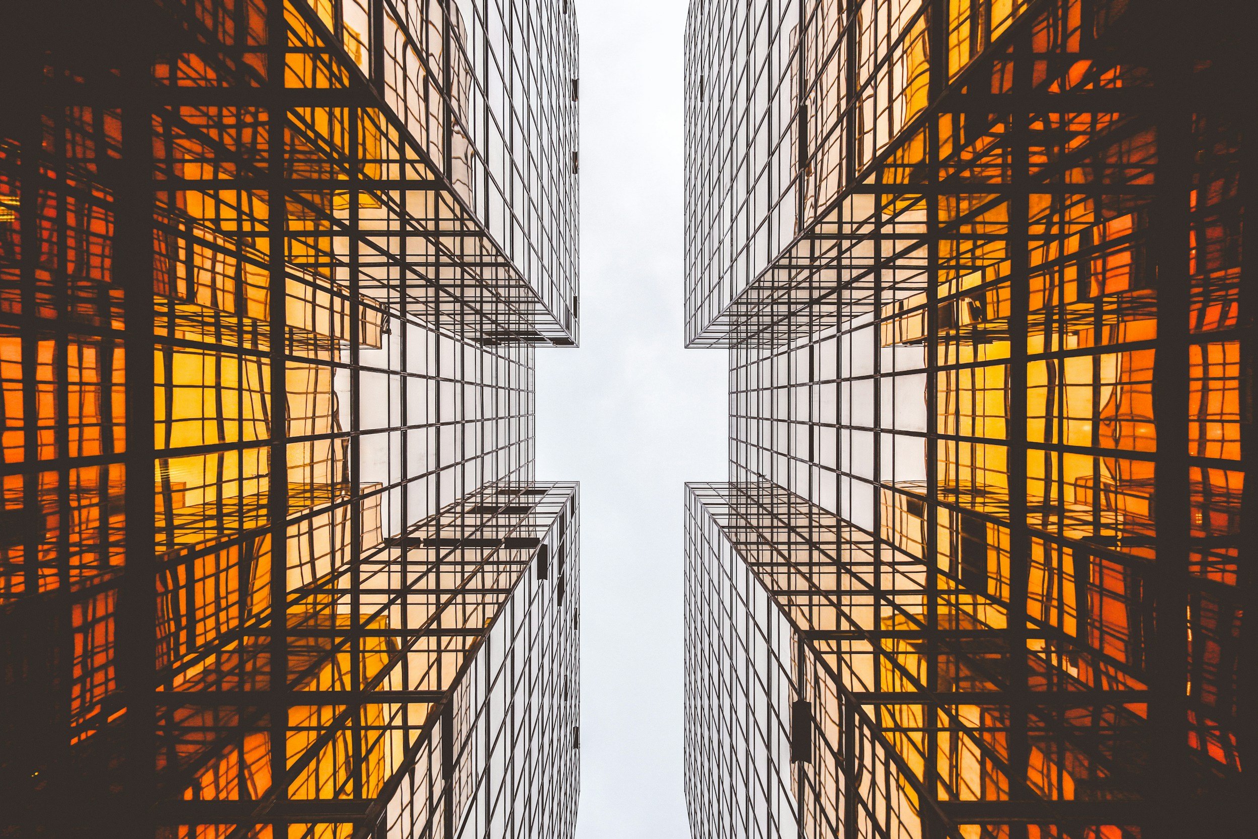 Looking up at two mirrored office buildings with glass facades reflecting the sky and surrounding structures.