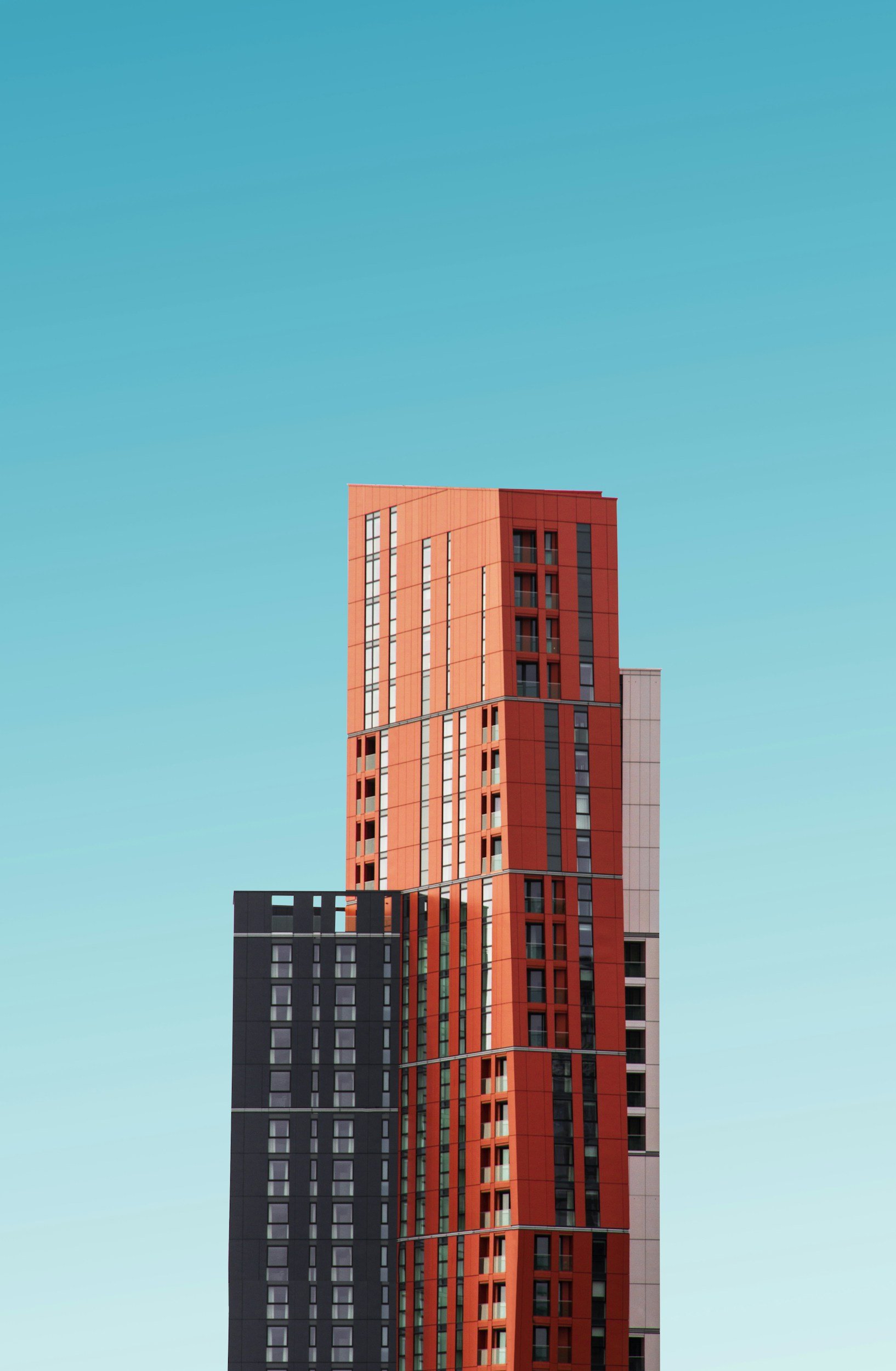 A tall, modern skyscraper with a mix of red, black, and white panels, set against a clear blue sky.