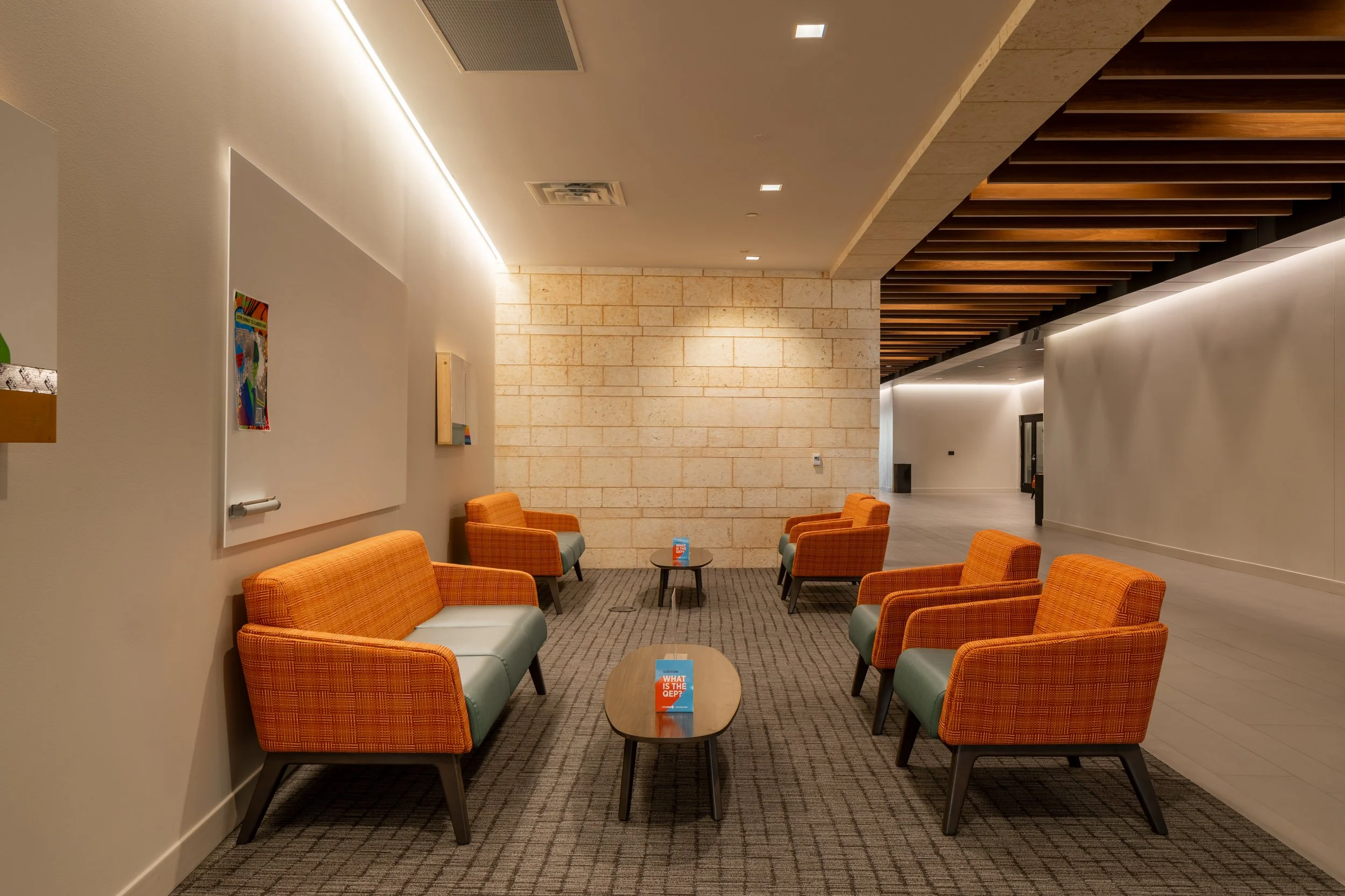 A modern interior waiting area with orange chairs, small tables with informational pamphlets, a whiteboard, and contemporary wall and ceiling design.