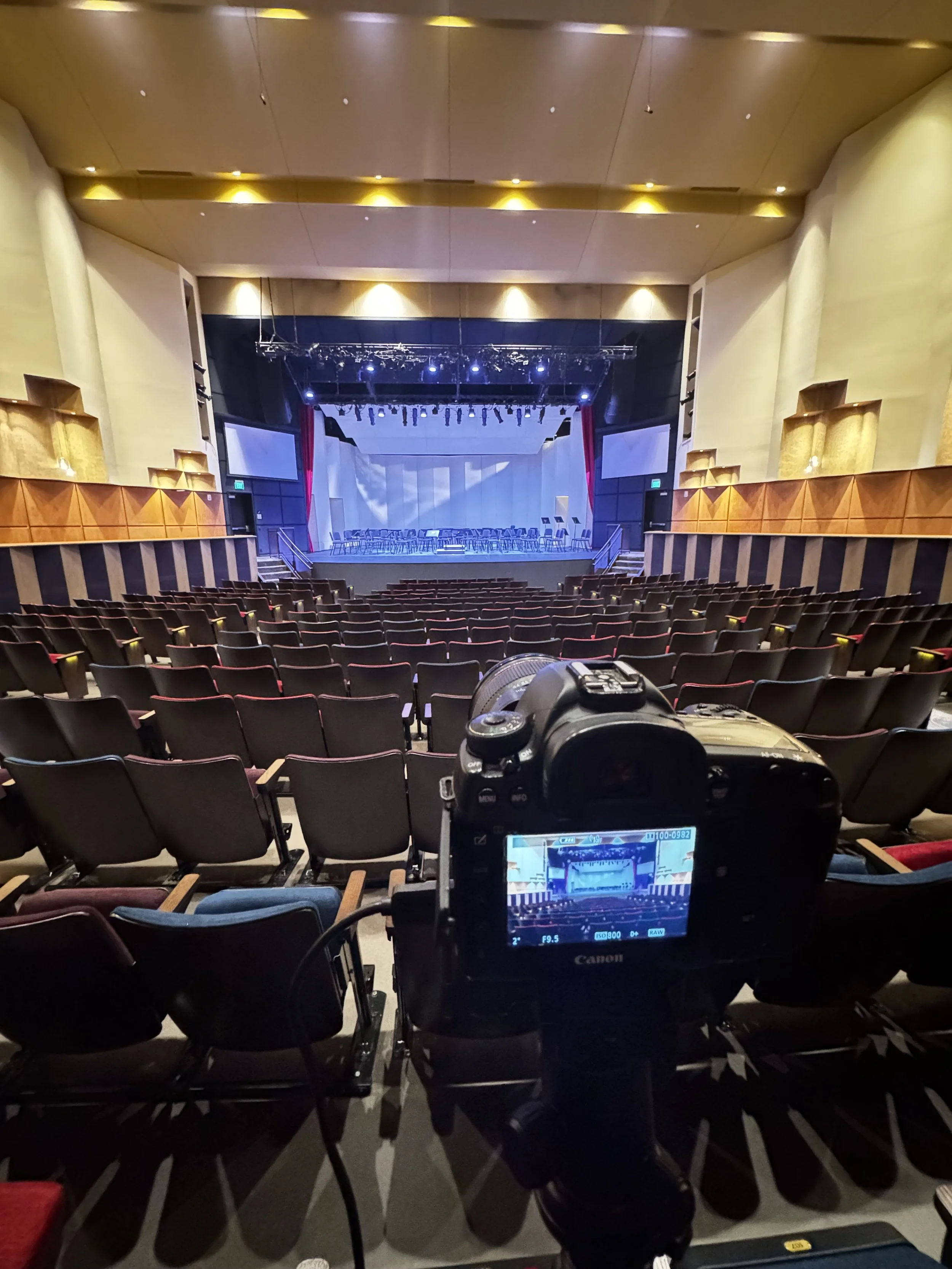 Empty theater with a stage, rows of seats, and a camera focused on the stage for filming or photography.