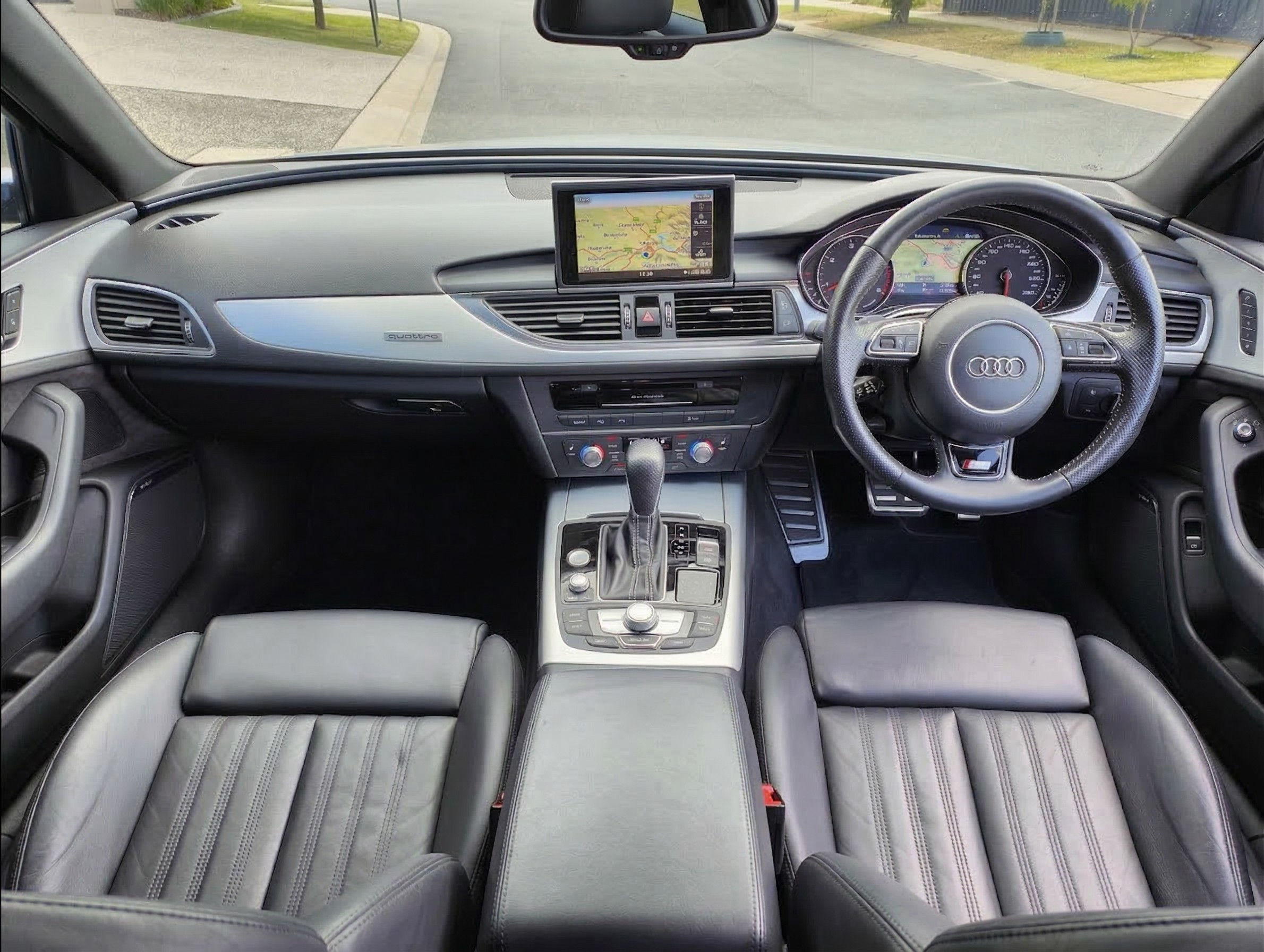 Interior of an Audi vehicle, showing the dashboard, steering wheel, and front seats. The dashboard includes a navigation screen and various controls, with black leather seats and a gear shift in the center console.