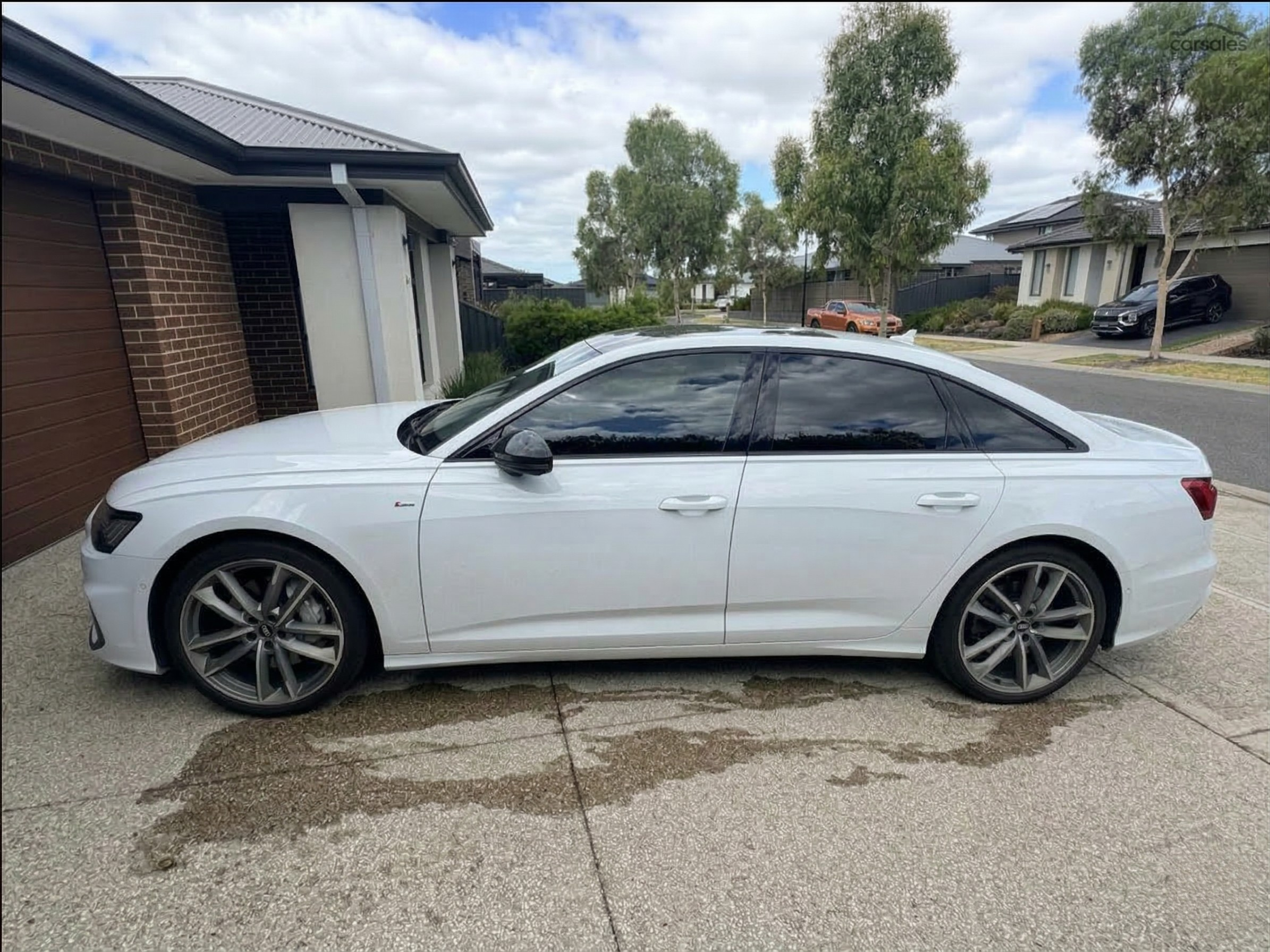 A white sedan parked in a residential driveway with water puddles on the concrete surface.