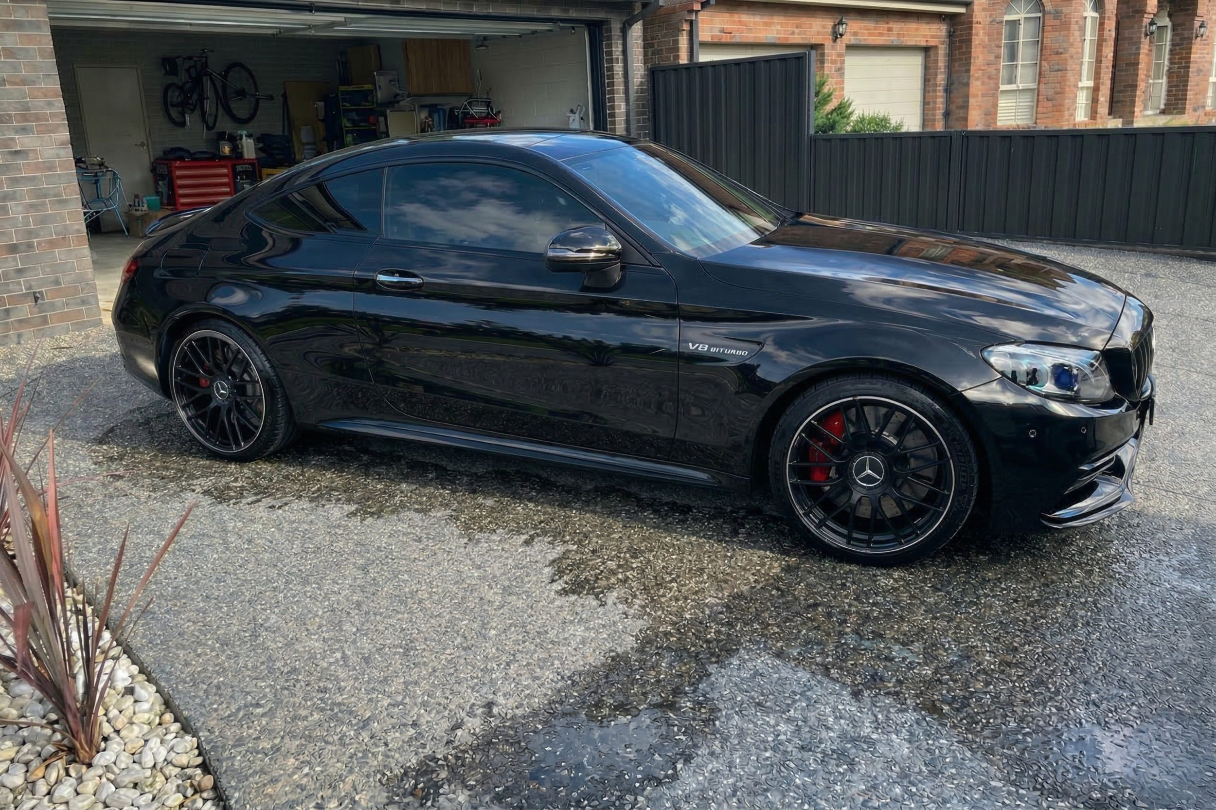 Black Mercedes-Benz coupe parked on a driveway with a garage in the background.
