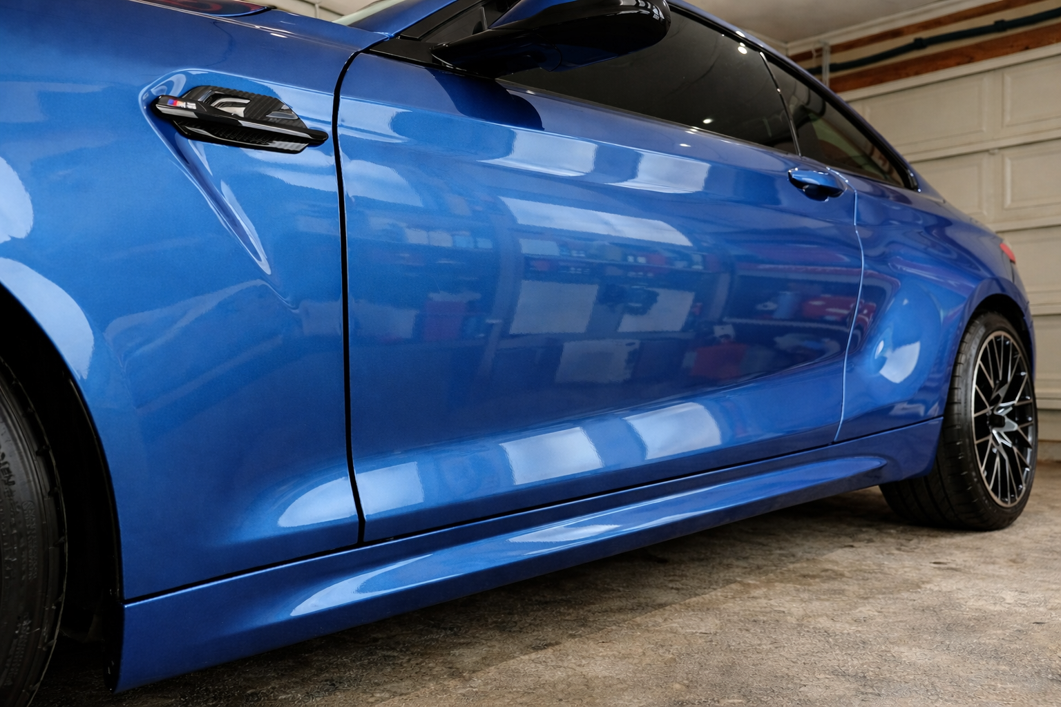 Close-up of a blue sports car with black side mirror and black wheels inside a garage.