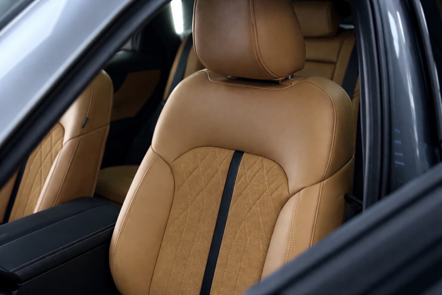 Inside view of a car with tan leather seats and headrests, black seatbelt, and black interior door frame.