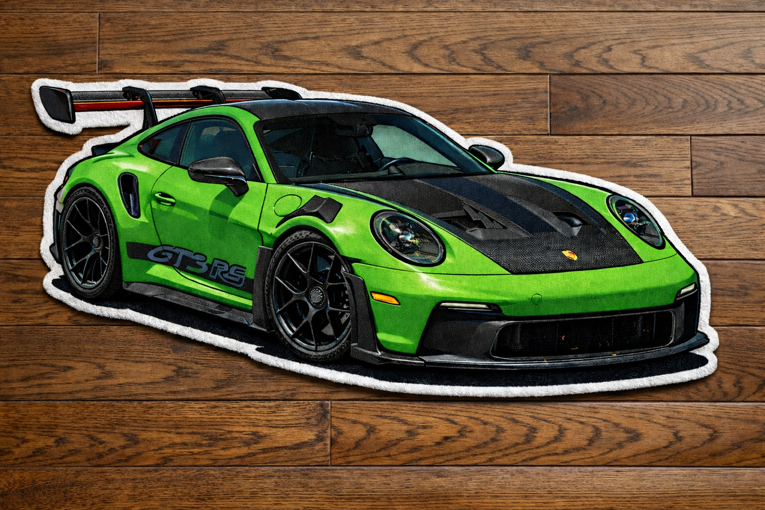 A green scale model of a Porsche 911 GT3 RS sports car with black accents, placed on a wooden floor.