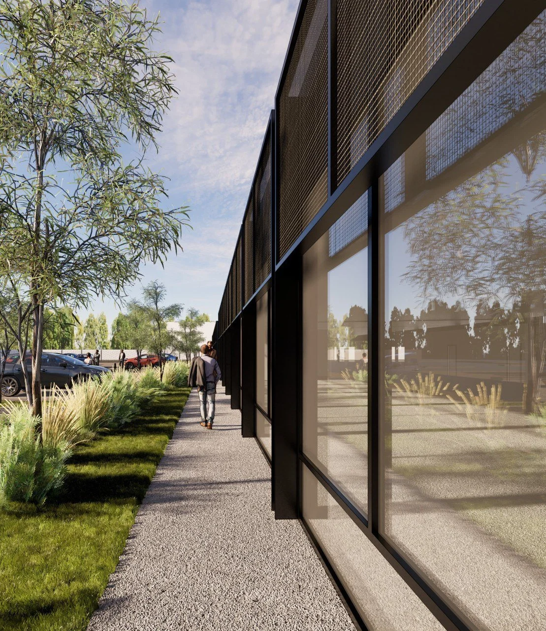 A modern building with reflective glass windows reflects trees and sky. A sidewalk runs alongside, bordered by landscaped greenery, with a person walking.