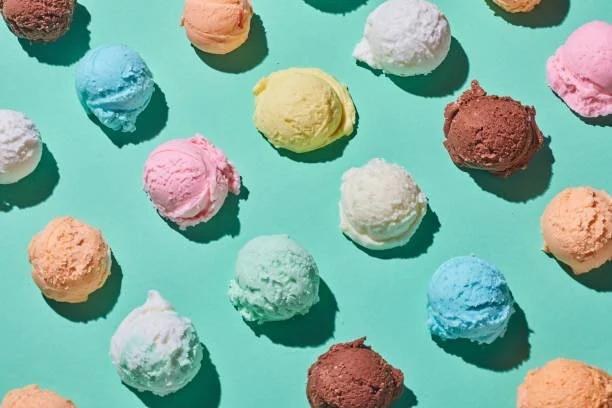 Colorful scoops of various ice cream flavors on a light turquoise background.