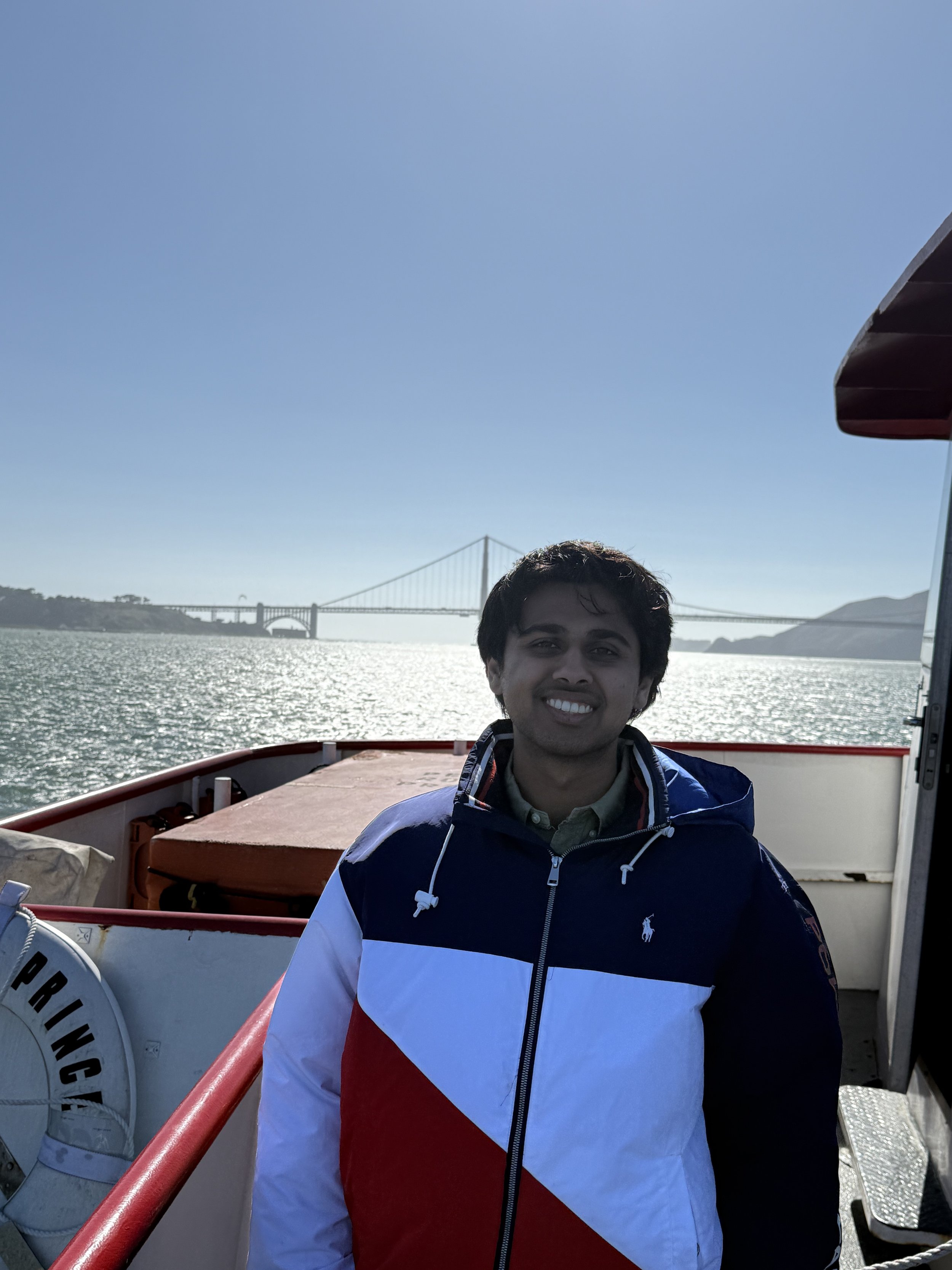 A young man smiling on a boat with water and a bridge in the background.
