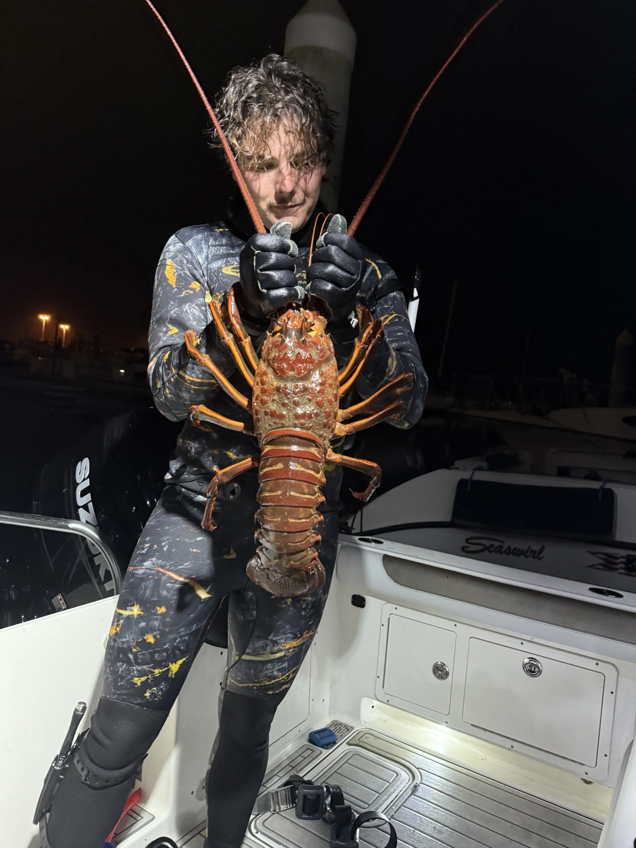 Person holding a large lobster on a boat at night.