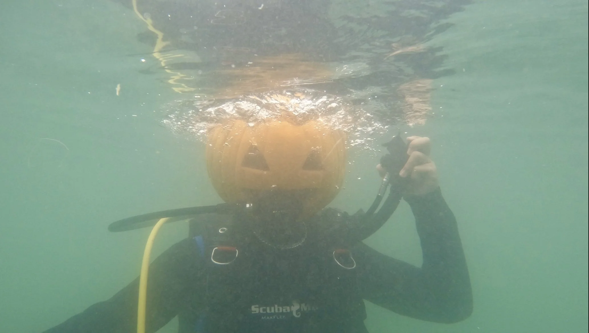 Scuba diver underwater holding a camera, with a yellow diving helmet or helmet-like object in front of them