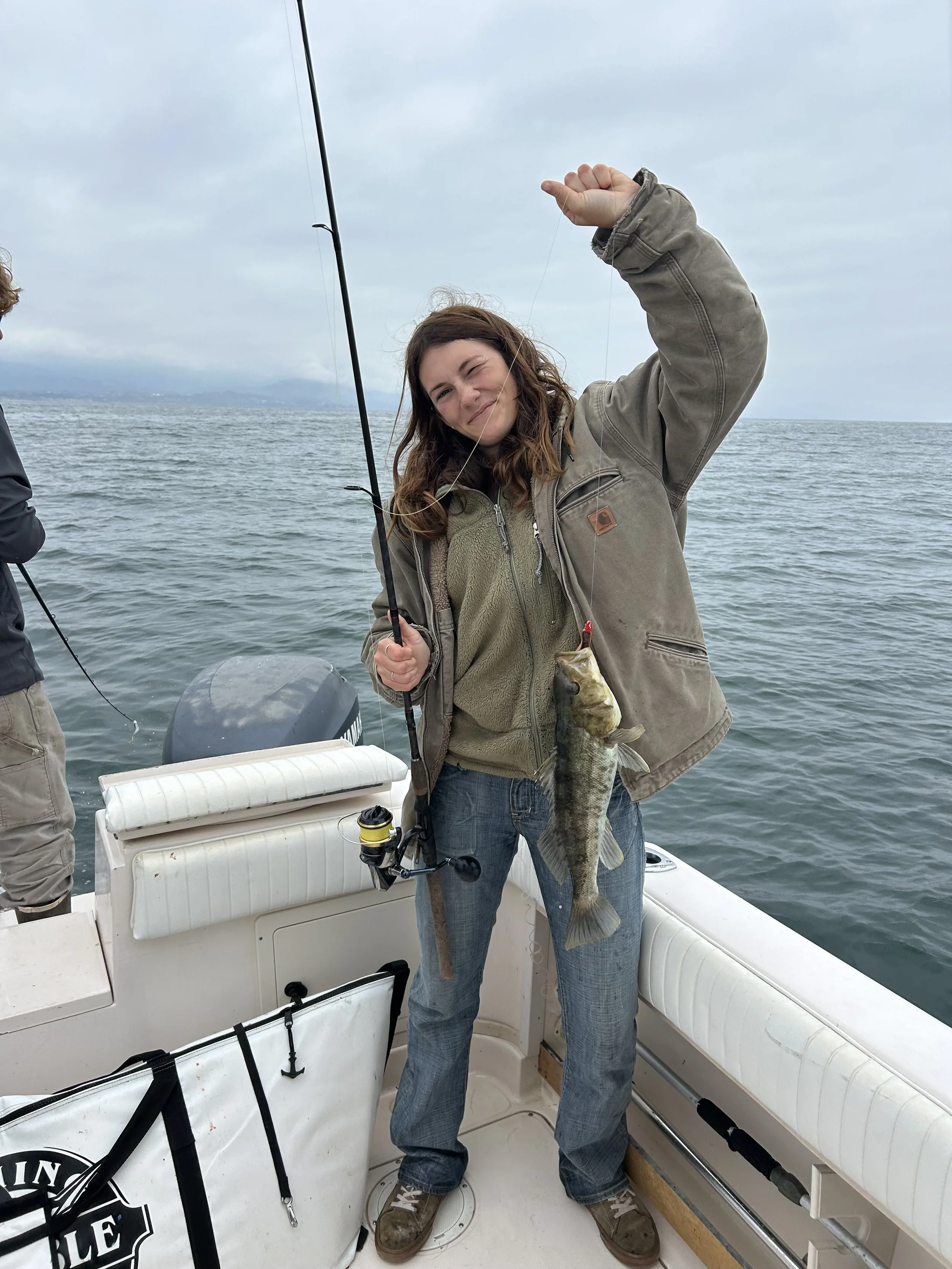 A woman on a boat holding a large fish she caught with a fishing rod.