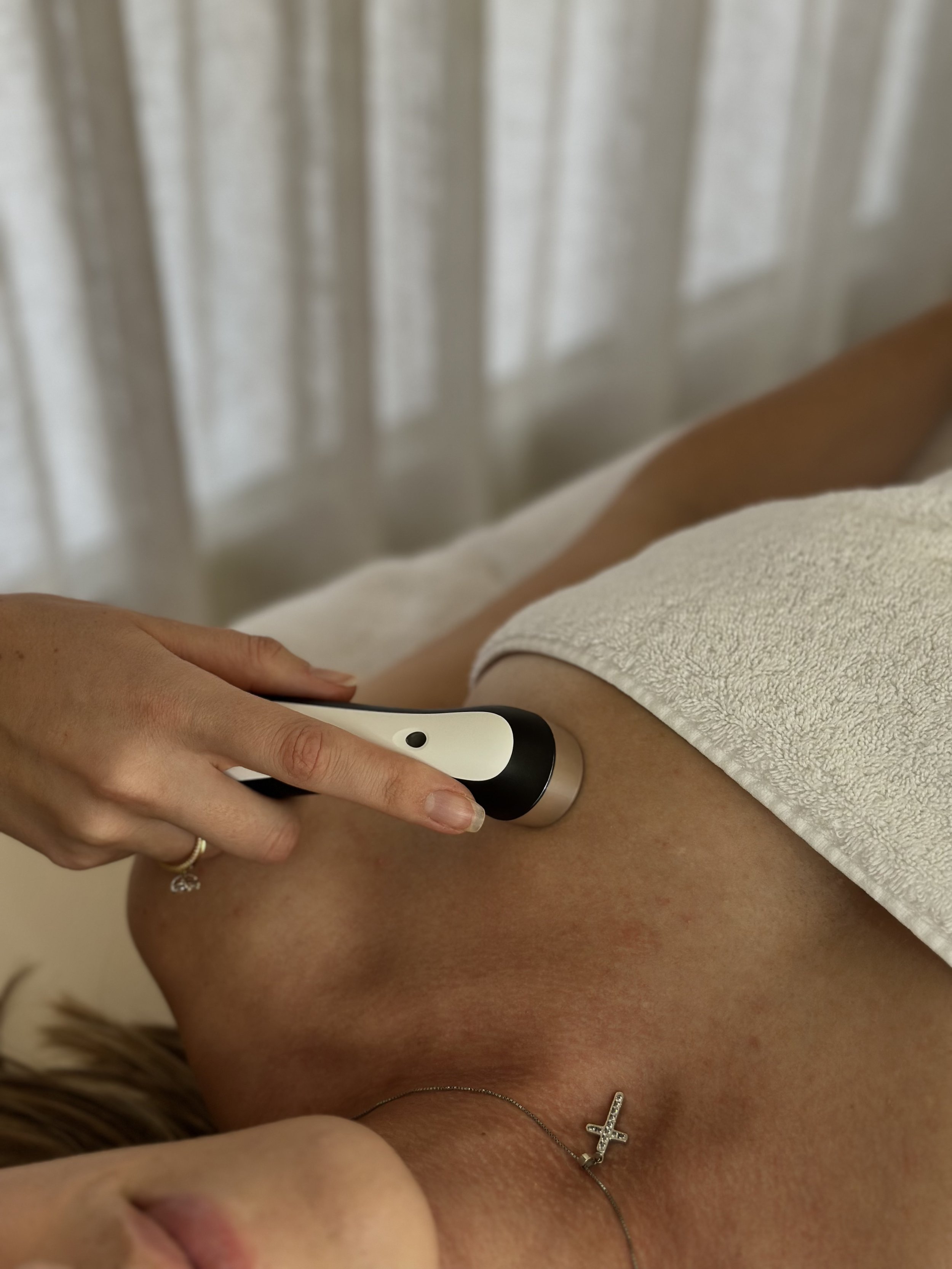 A person receiving a medical treatment on their arm with a handheld device, with another person holding the device, in a clinical setting.