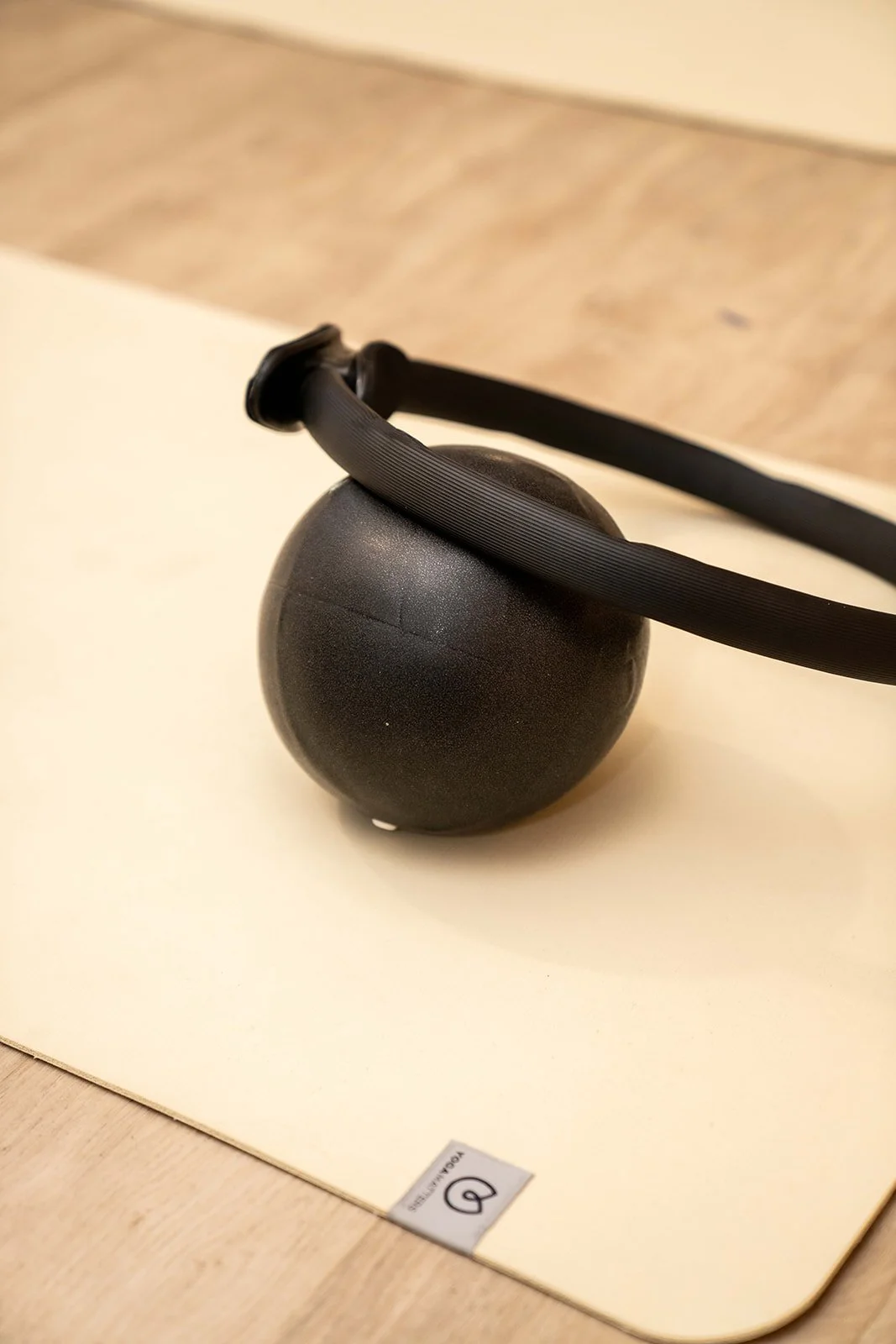 A black kettlebell with a wider base, sitting on a white surface with a black strap coiled around it.