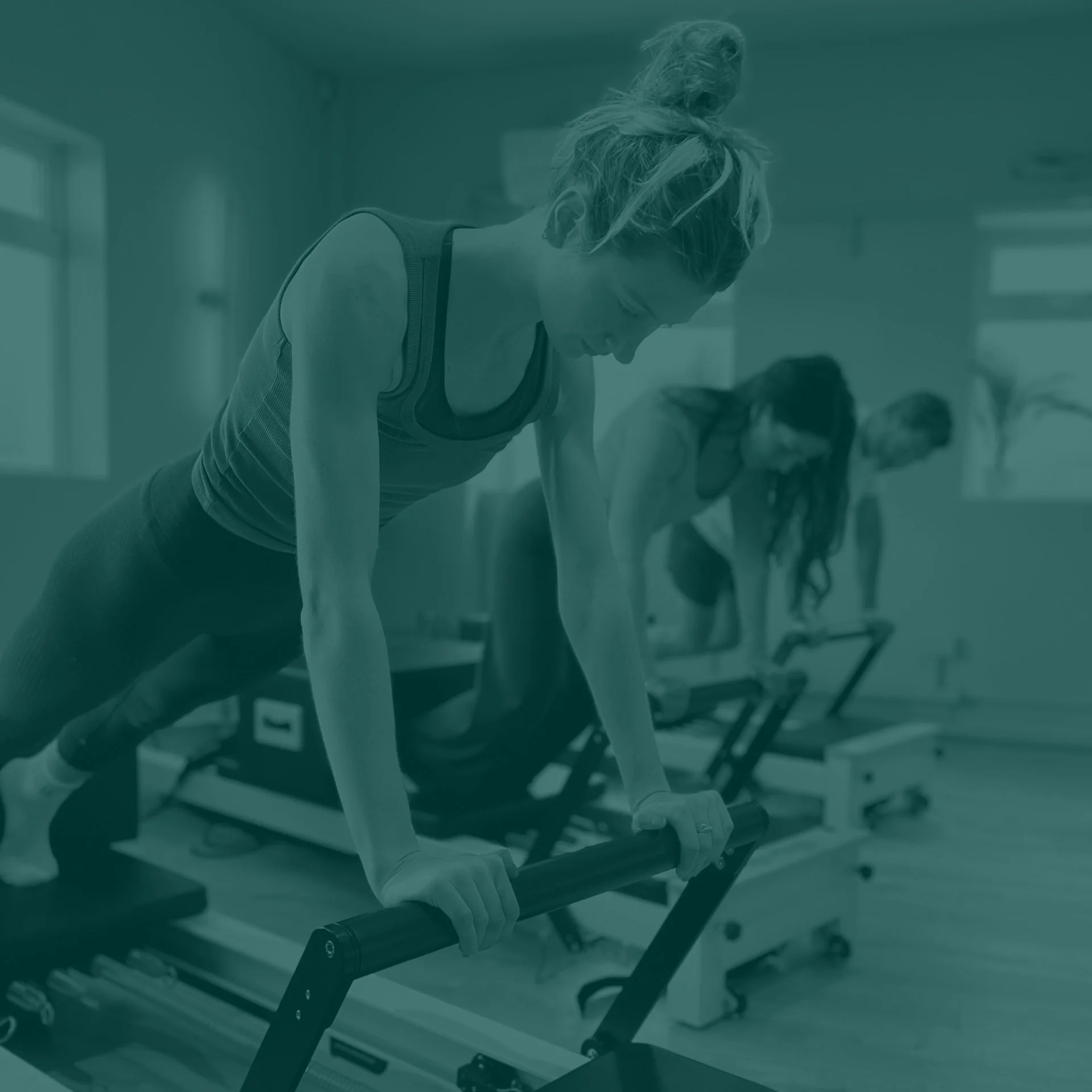 A woman using a push-up board in a Reformer Pilates class with other women in the background.