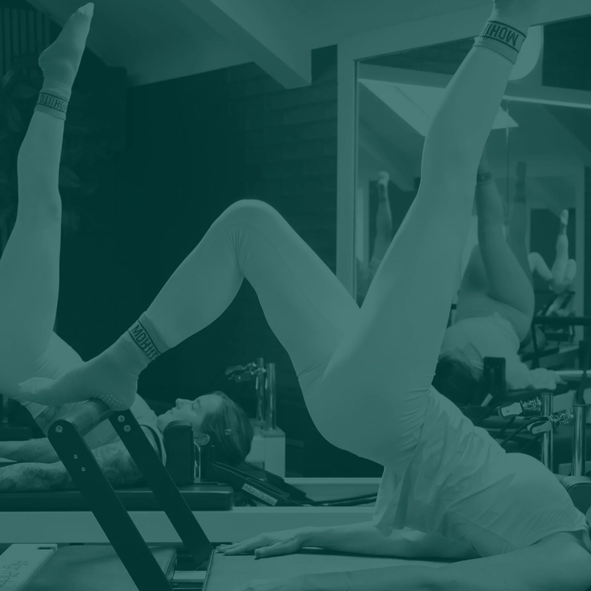 Two women engaging in a pilates exercise on specialized equipment in a fitness studio.