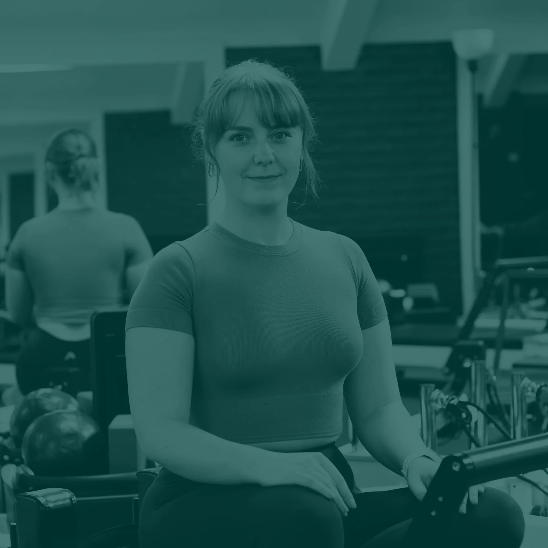 Woman with red hair in a gym, sitting on a workout machine and smiling at the camera.