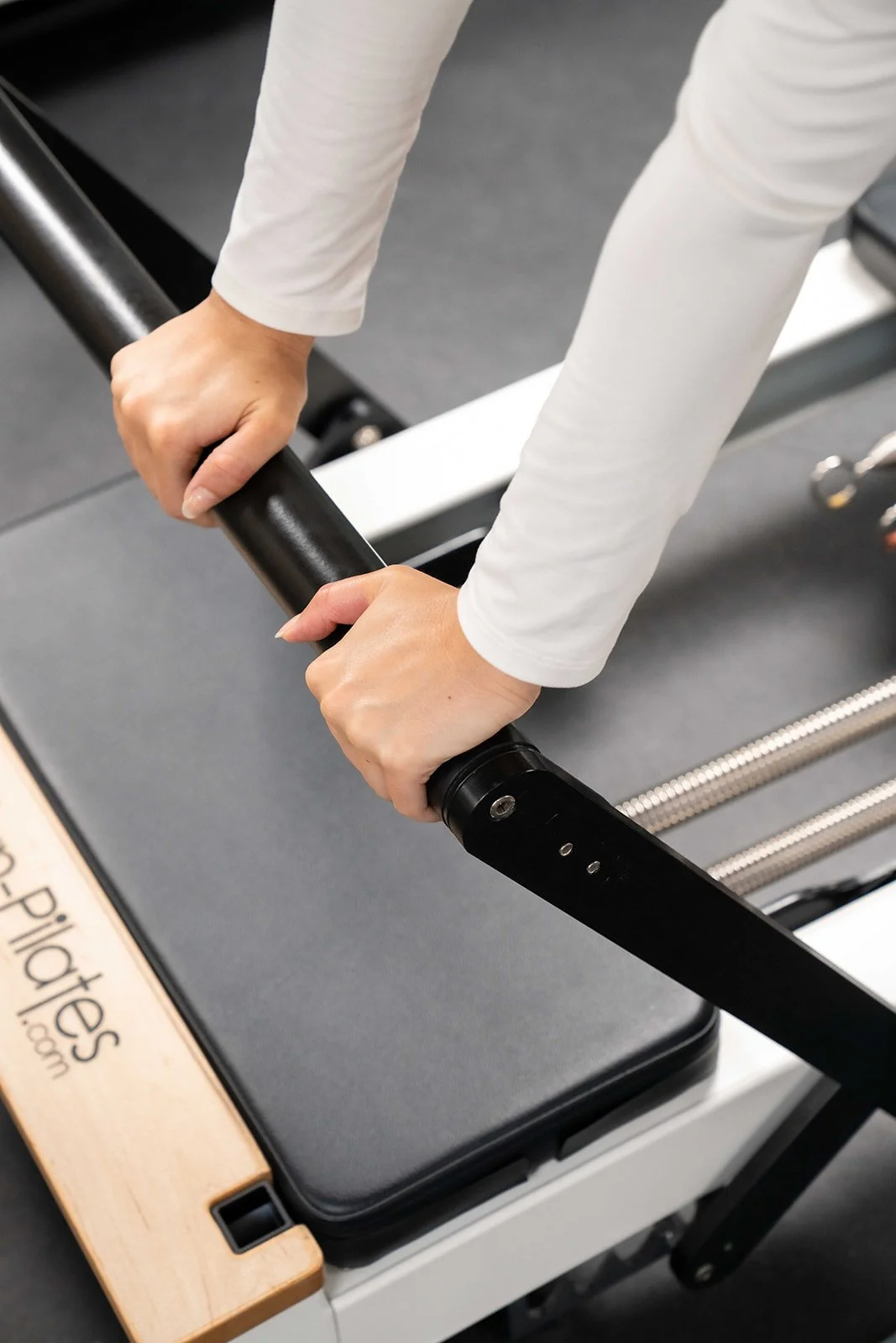 Person holding and adjusting a black Pilates reformer machine on a workout table.