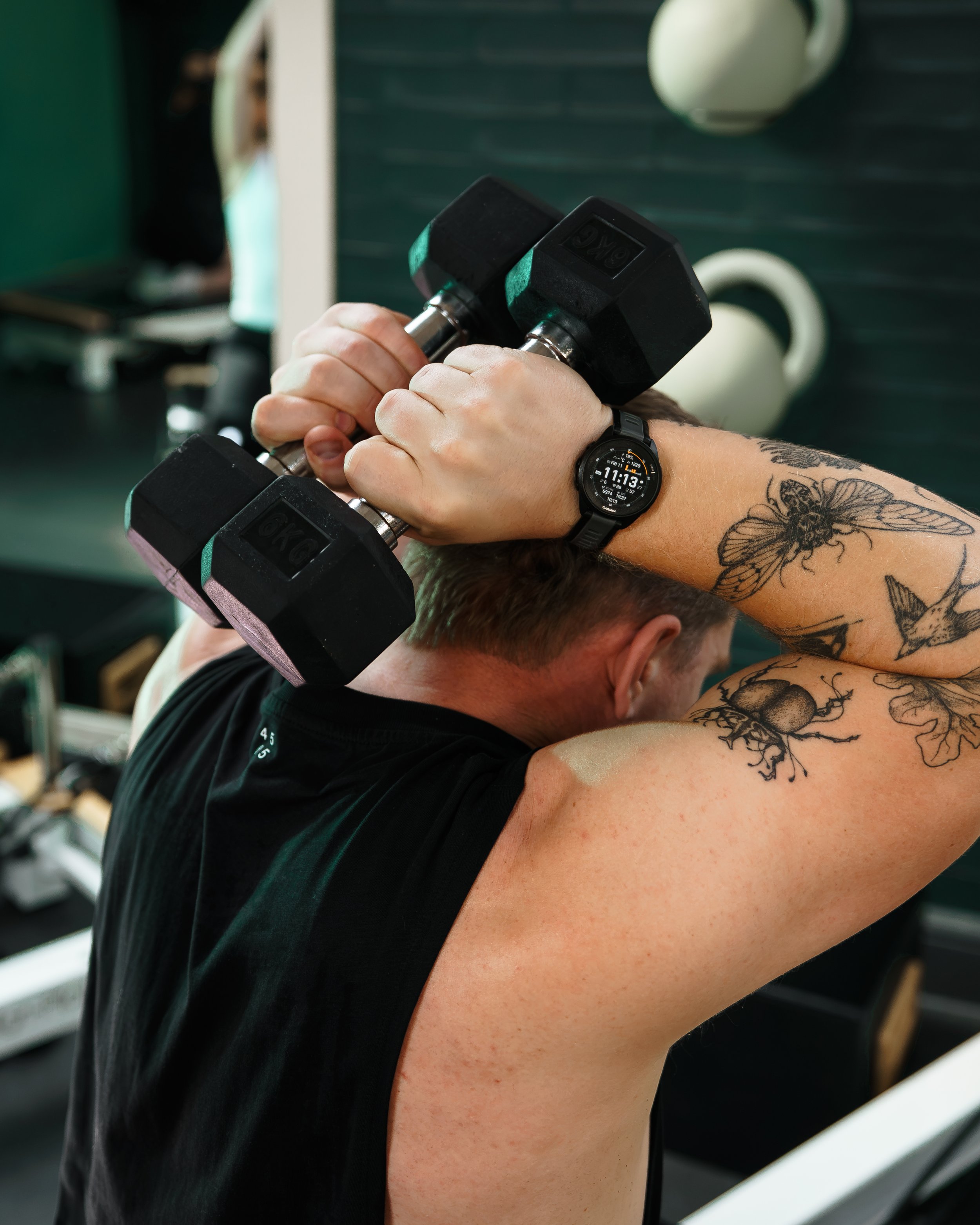 Person doing a workout with dumbbells on a yoga mat, wearing black leggings, white socks, and a black top.
