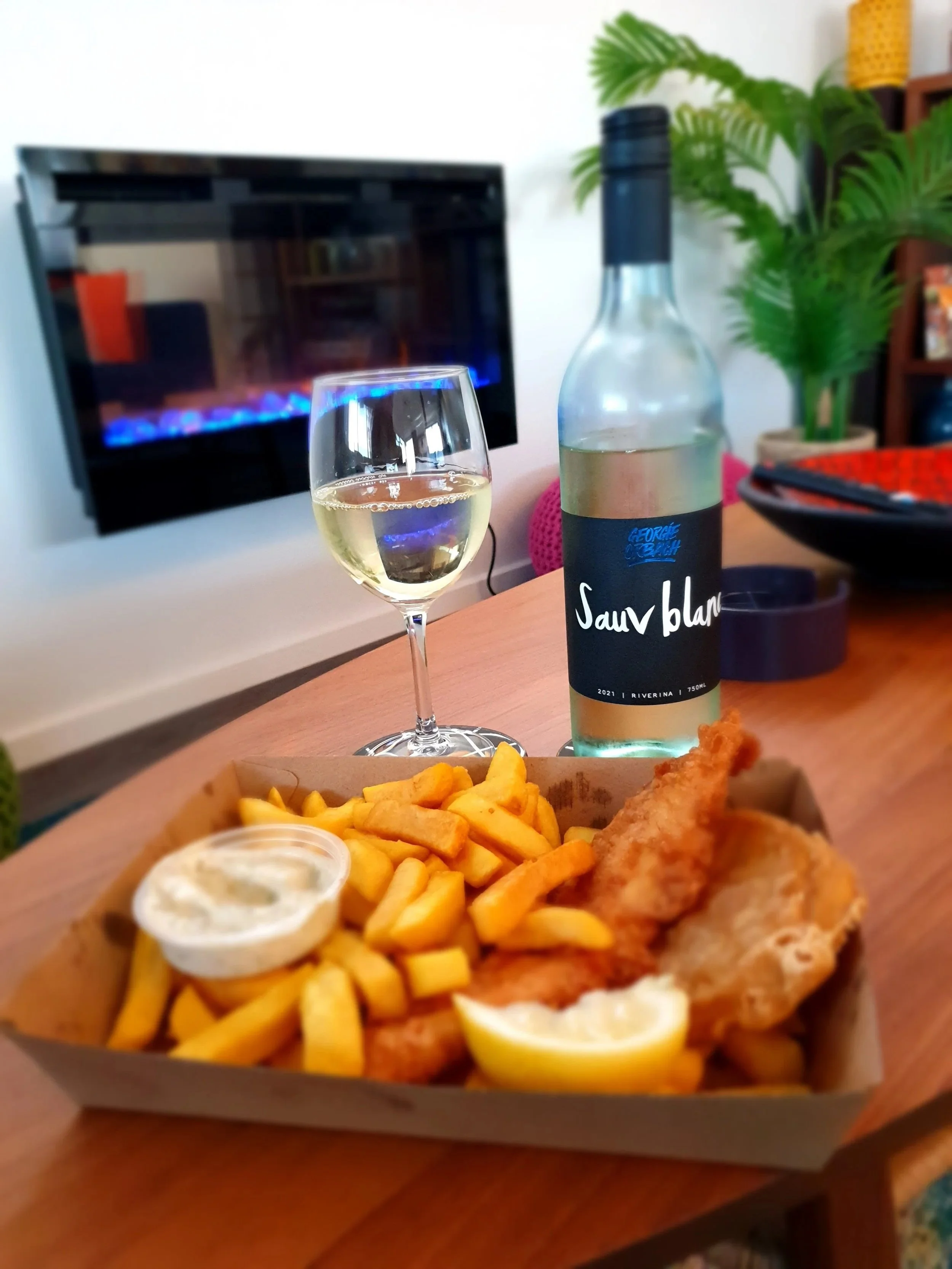 A view of the loungeroom downstairs featuring a meal of fish and chips and a glass of Georgie Orbach Sauv Blanc. 