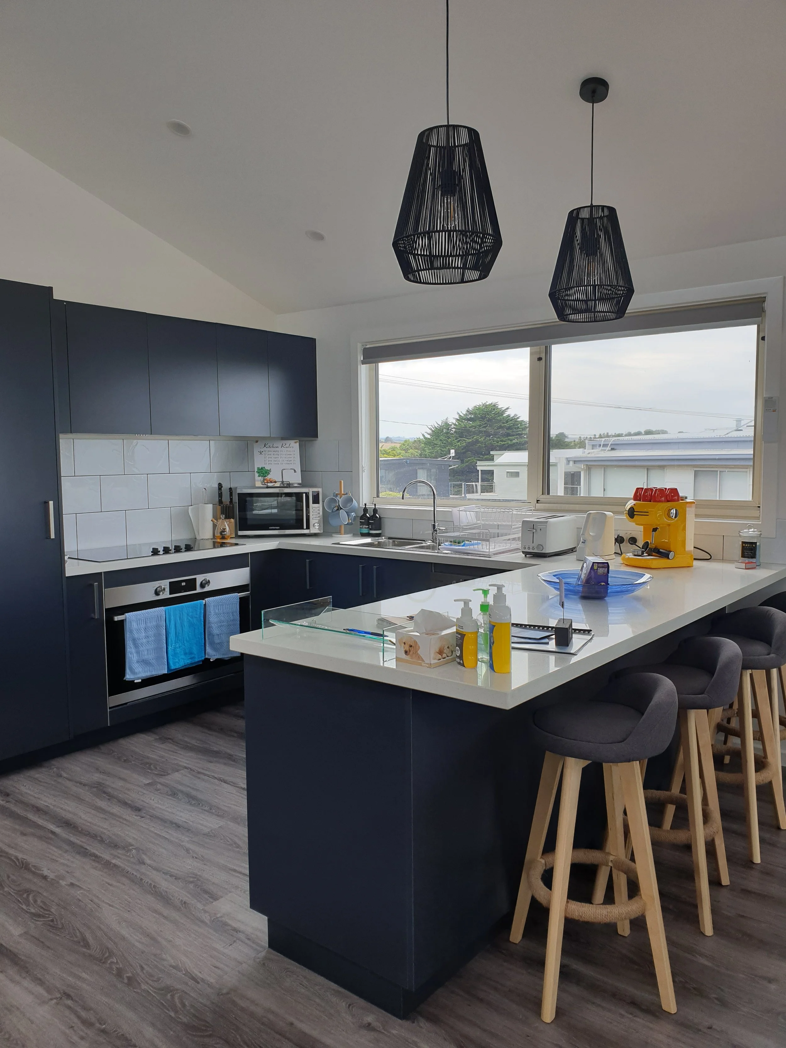 A view of the kitchen showcasing all the benches, oven and windows looking out toward the deck.
