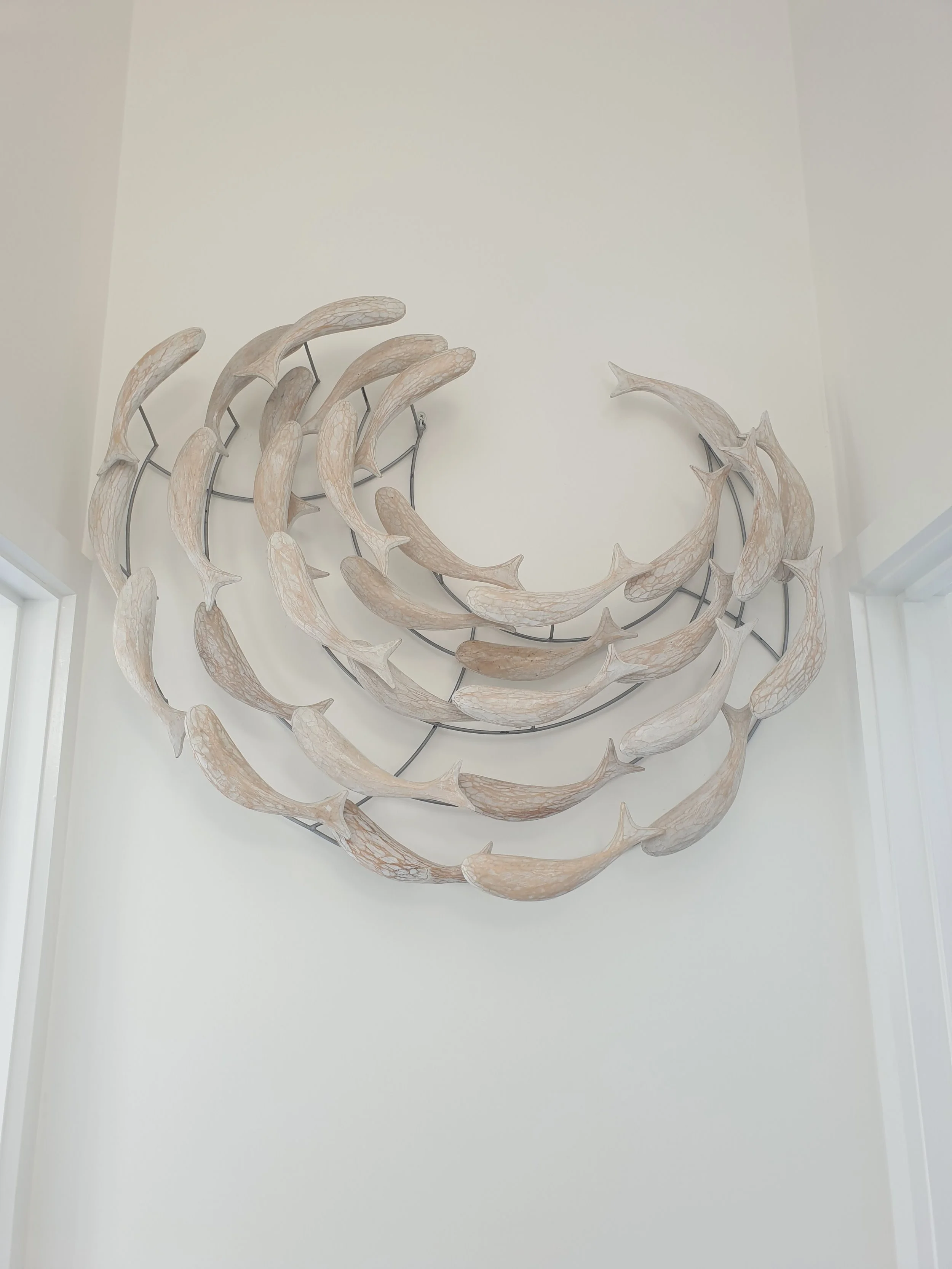 Wall sculpture of multiple decorative shark fins arranged in a circular pattern on the white wall.
