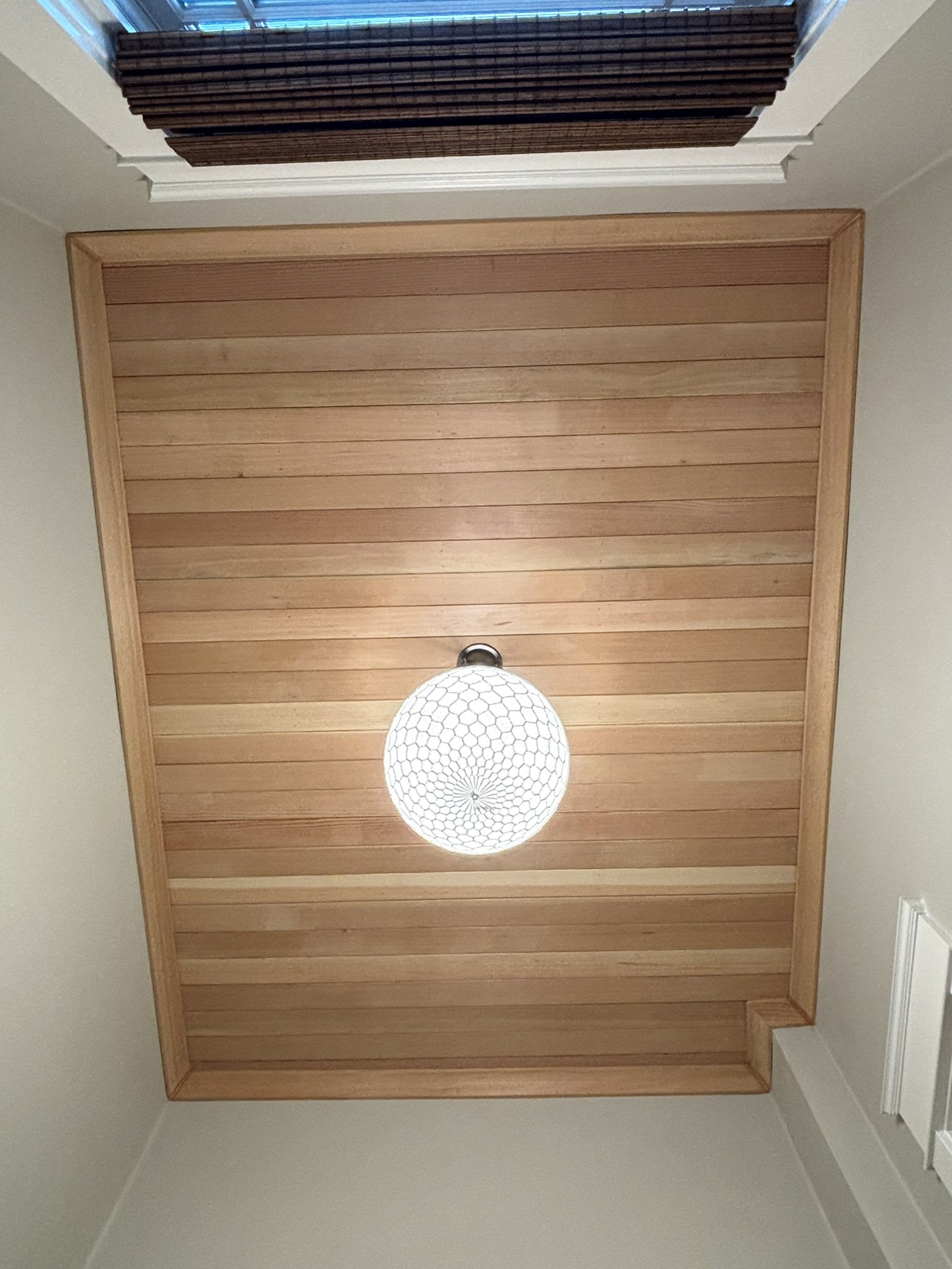 Ceiling with wooden paneling and a hanging light fixture with a honeycomb pattern