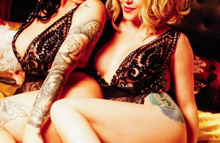 Close-up of two people in sequined clothing sitting together, showing tattoos on arms and thighs.