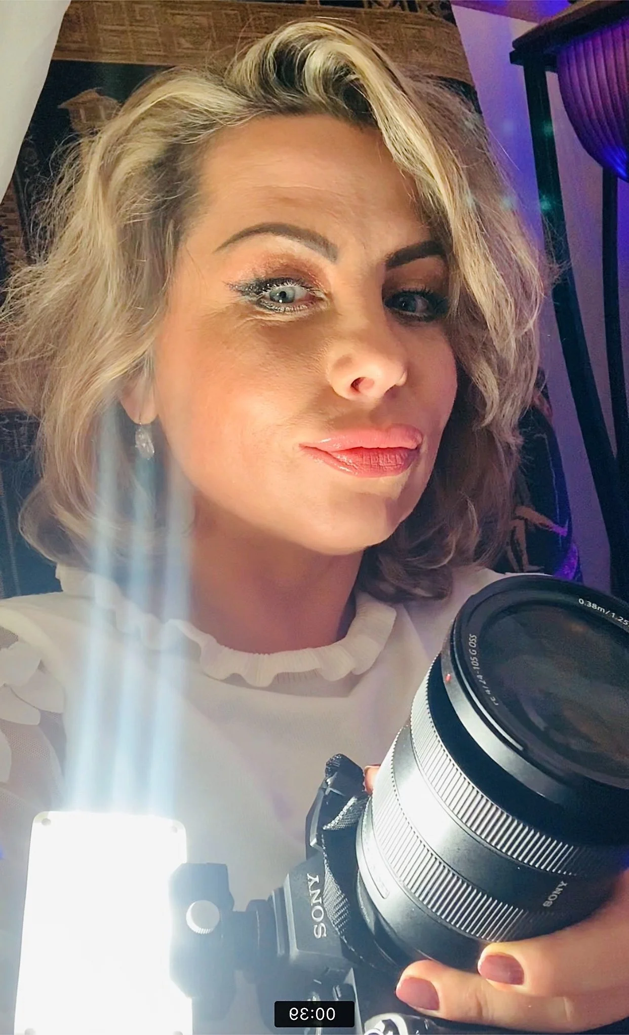 Person holding a Sony camera with a bright light, in a close-up selfie.