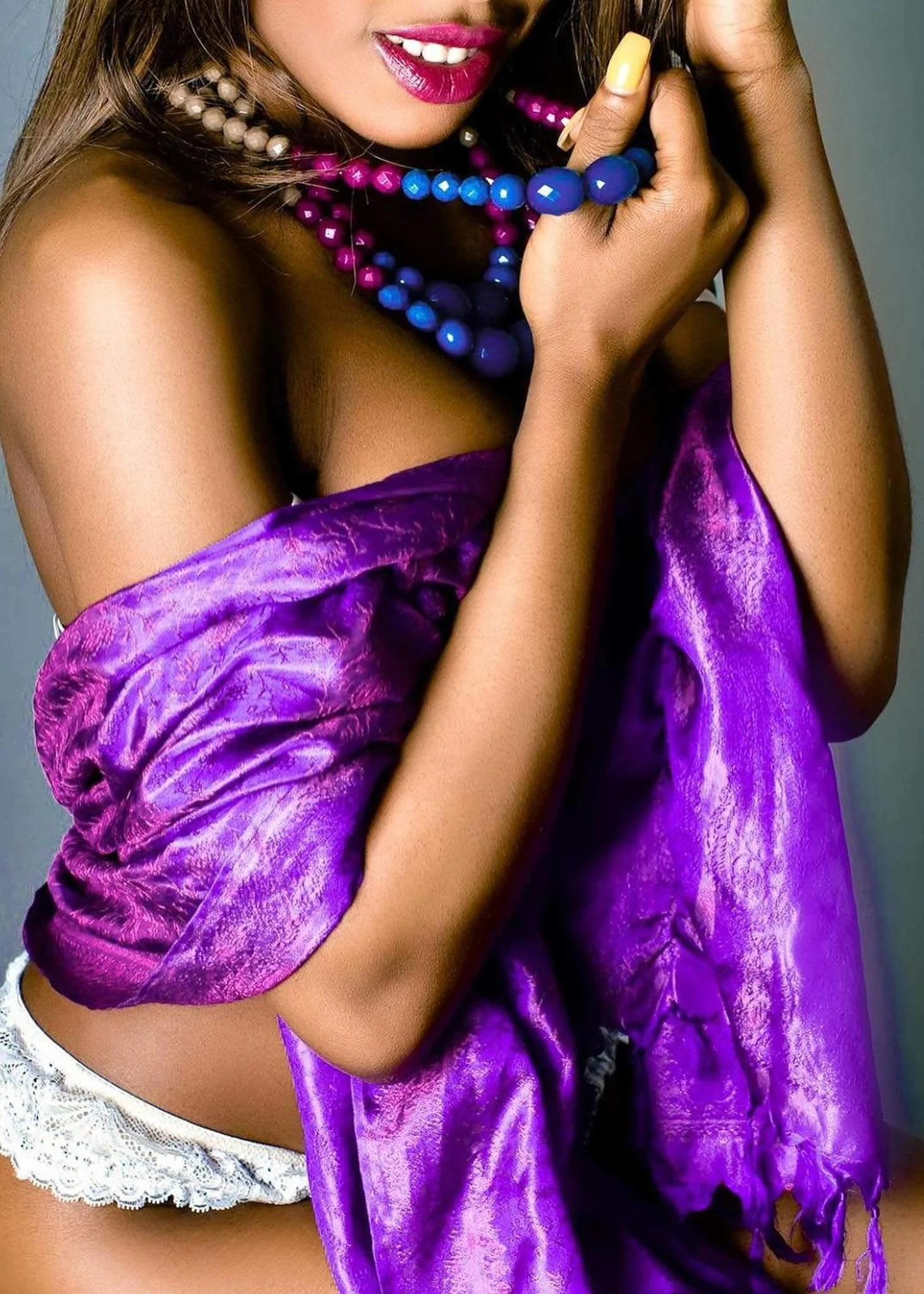 Close-up of a woman wearing colorful jewelry and a purple satin garment, with bright pink lipstick and a partial view of her face.