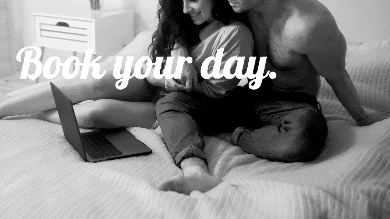 Couple sitting on bed with laptop, text 'Book your day.'
