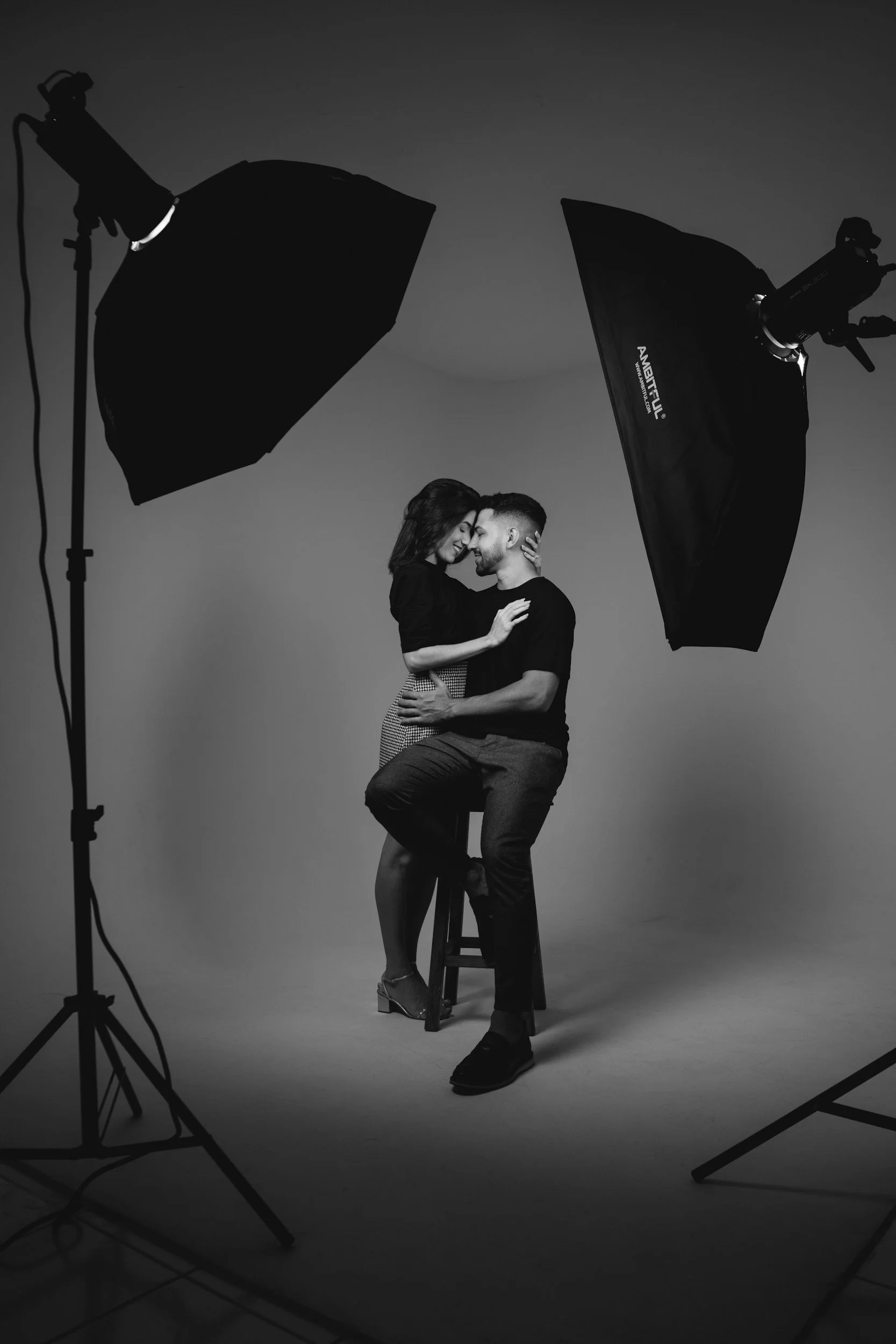 A man and woman are closely embracing in a photography studio with professional lighting equipment around them.