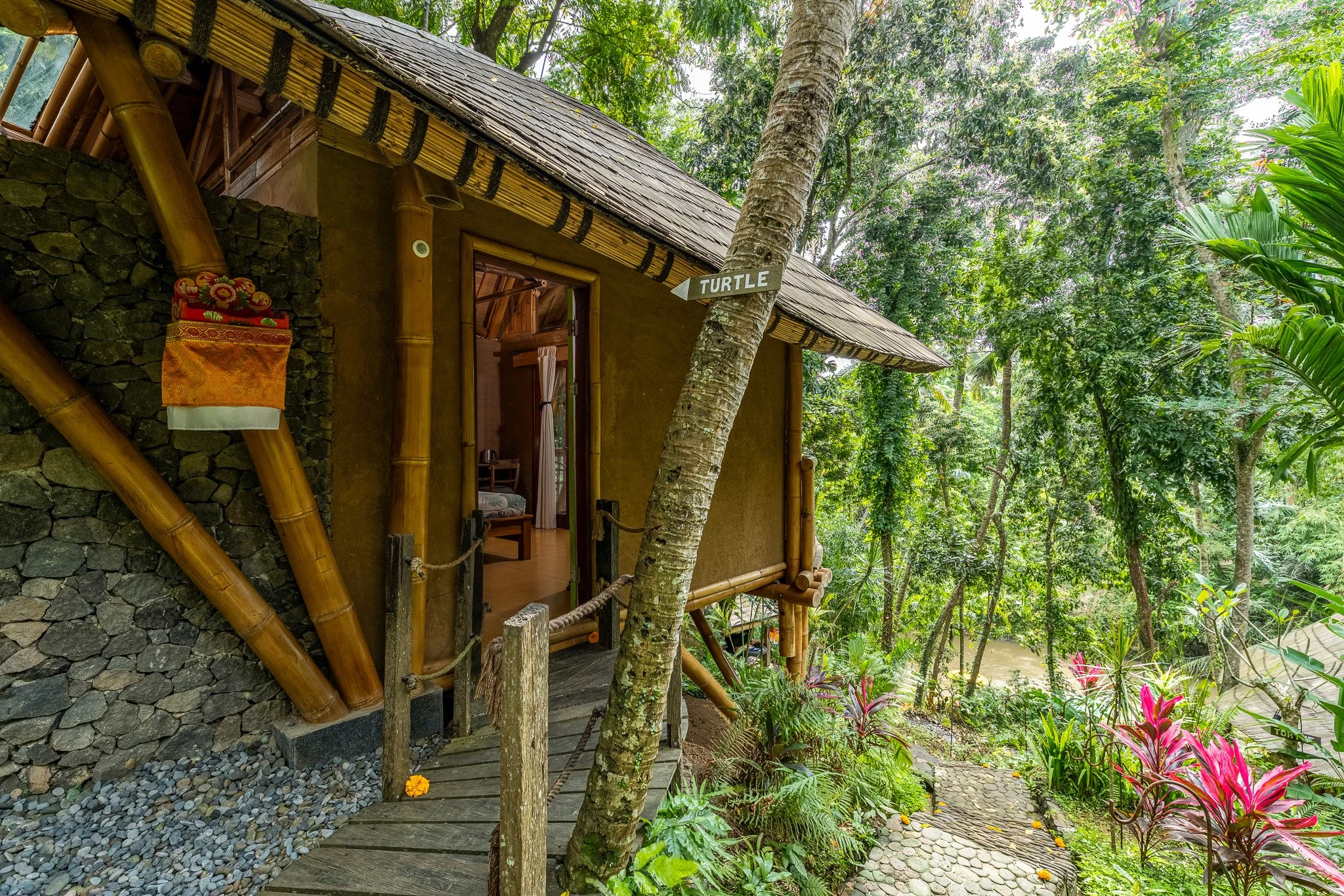 A treehouse with bamboo accents surrounded by lush tropical greenery, a pathway leading to the entrance, and a sign pointing to the turtle.