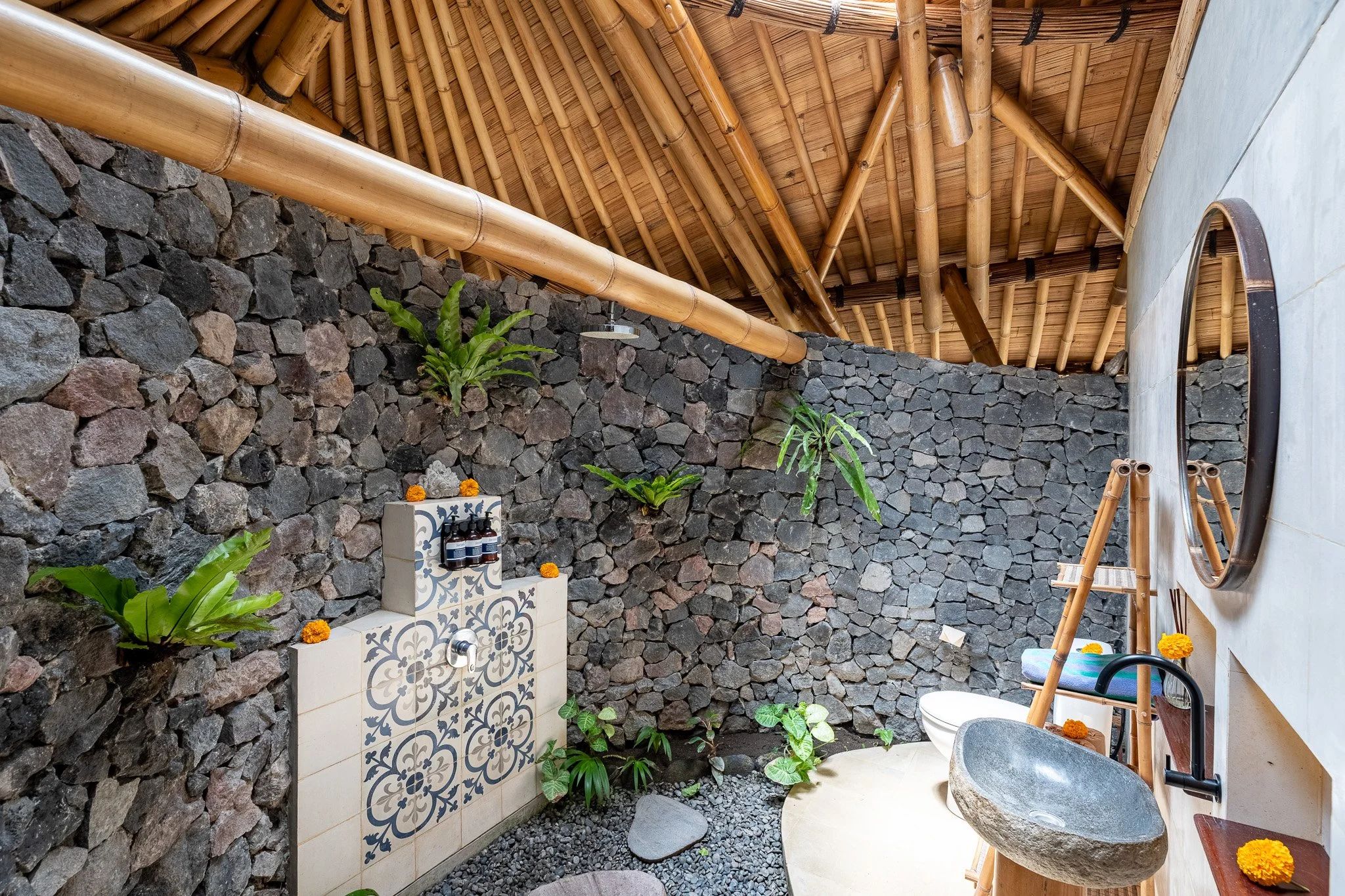 Indoor natural stone and bamboo bathroom with plants, a stone sink, a mirror, and decorative tiles.