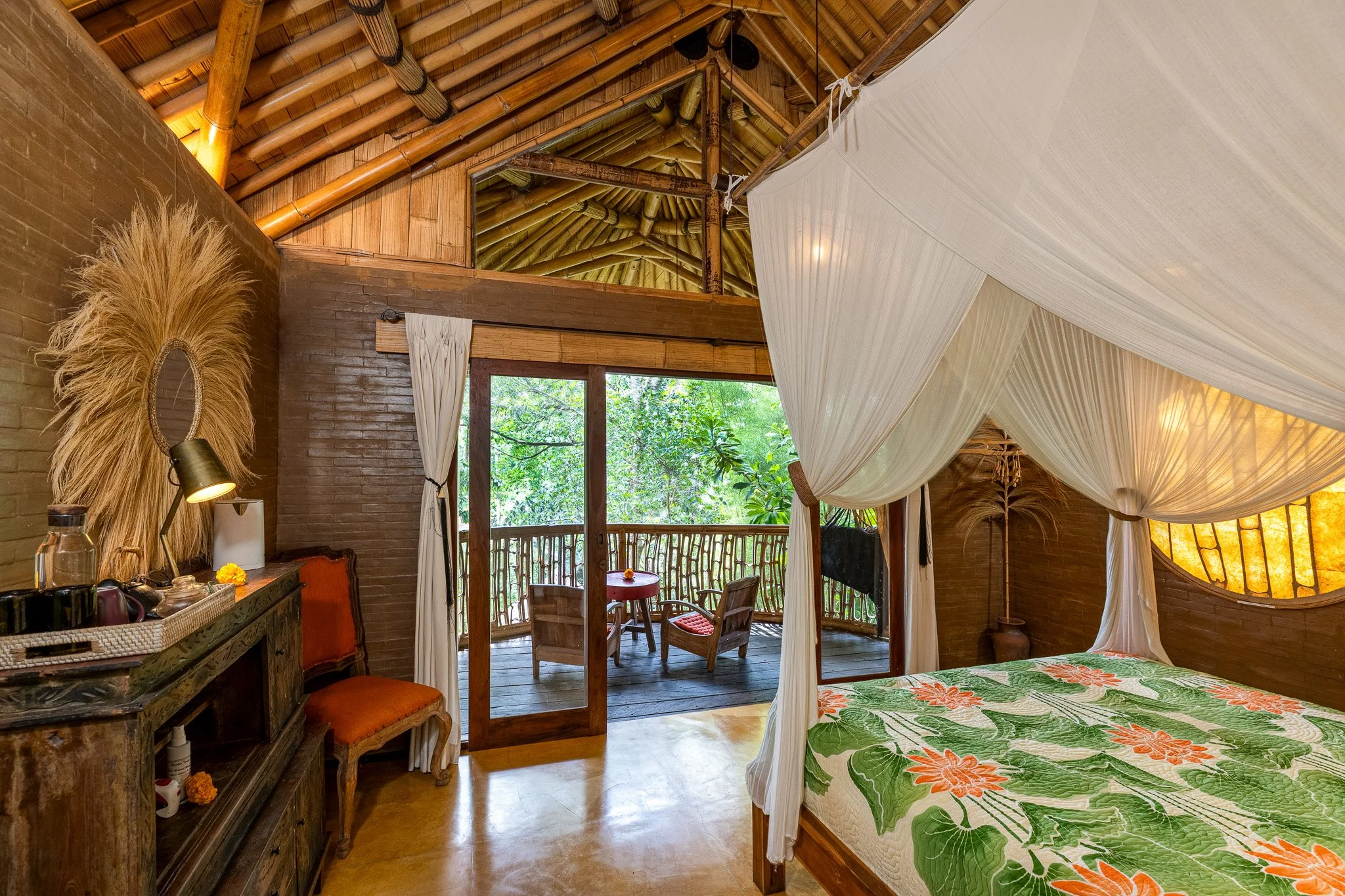 A rustic bedroom with a wooden ceiling and a balcony with outdoor seating, decorated with tropical and natural elements.