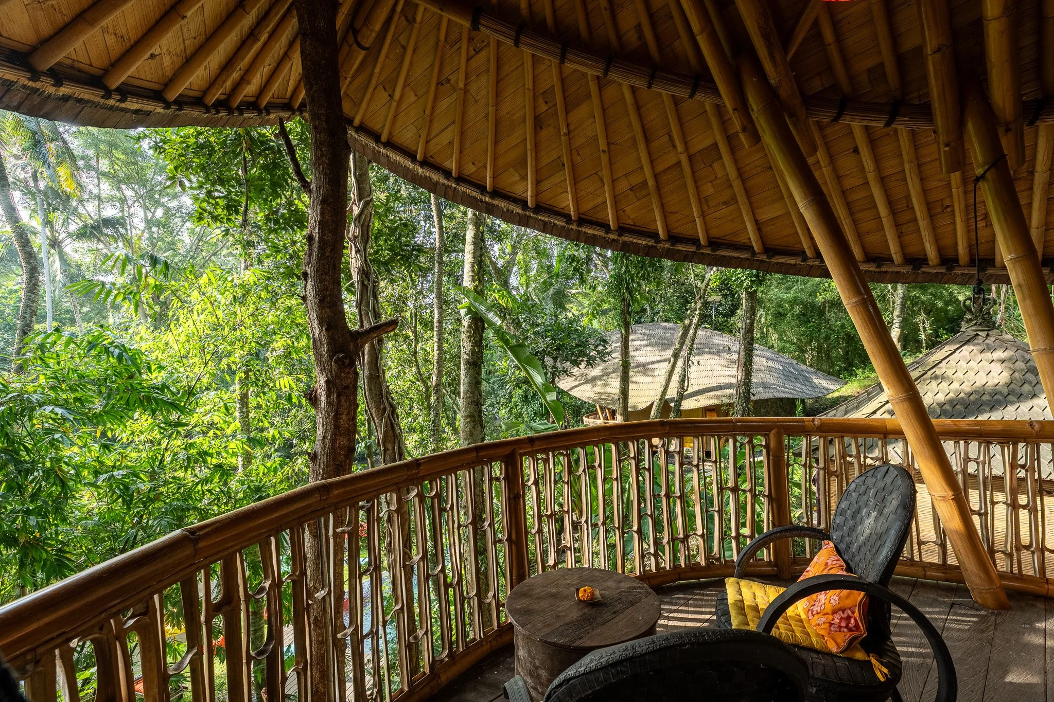 A wooden balcony with bamboo railing overlooking a lush tropical forest.
