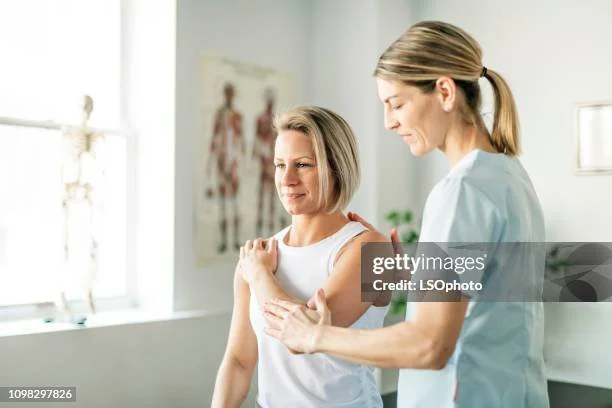 Physical therapist or healthcare professional examining a woman's shoulder in a medical setting.