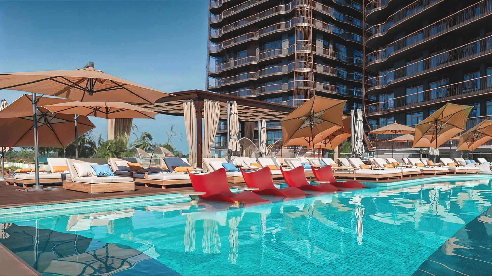 A swimming pool area with multiple lounge chairs and umbrellas, high-rise building in the background, and clear blue sky.