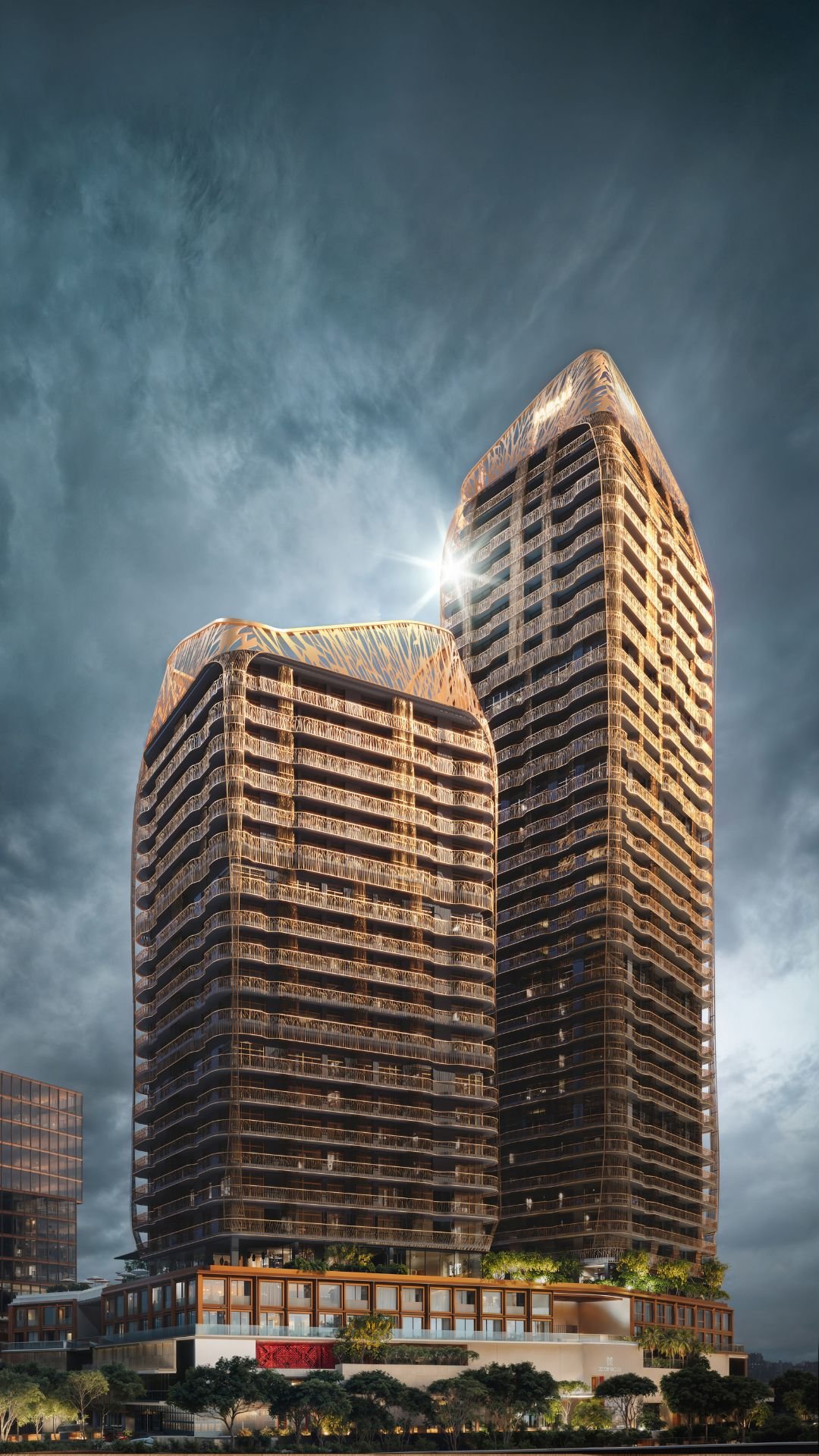 Two modern skyscrapers with curved designs and glass facades, with sunlight reflecting on the top of the taller building, set against a cloudy sky.