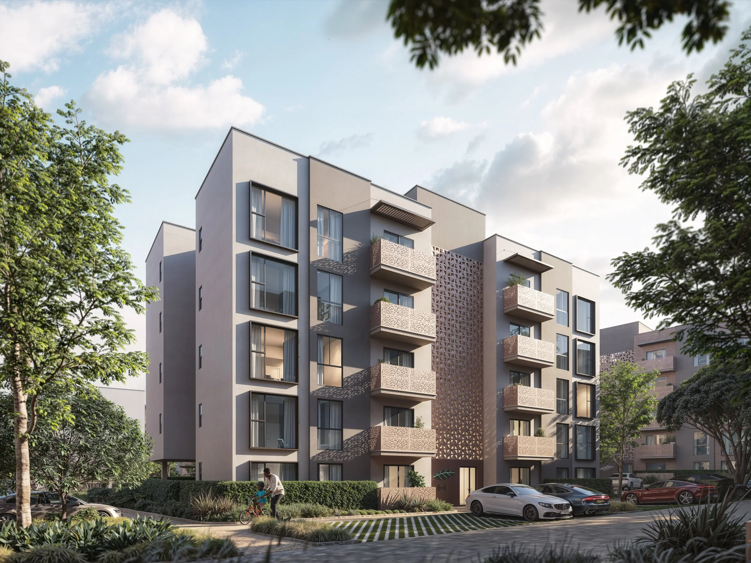 Modern white multi-story apartment building with balconies, surrounded by green trees, with cars parked in front and a man and child riding a bike on the sidewalk.