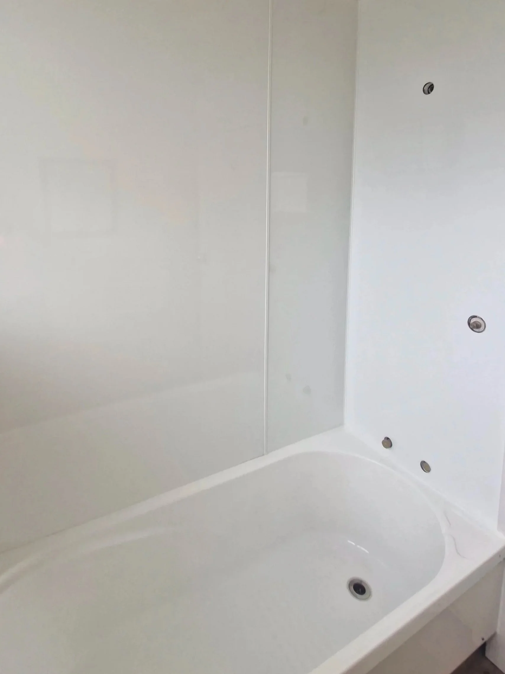 A white bathtub with a curved edge visible, situated against white walls with a glass shower door and small round fixtures.